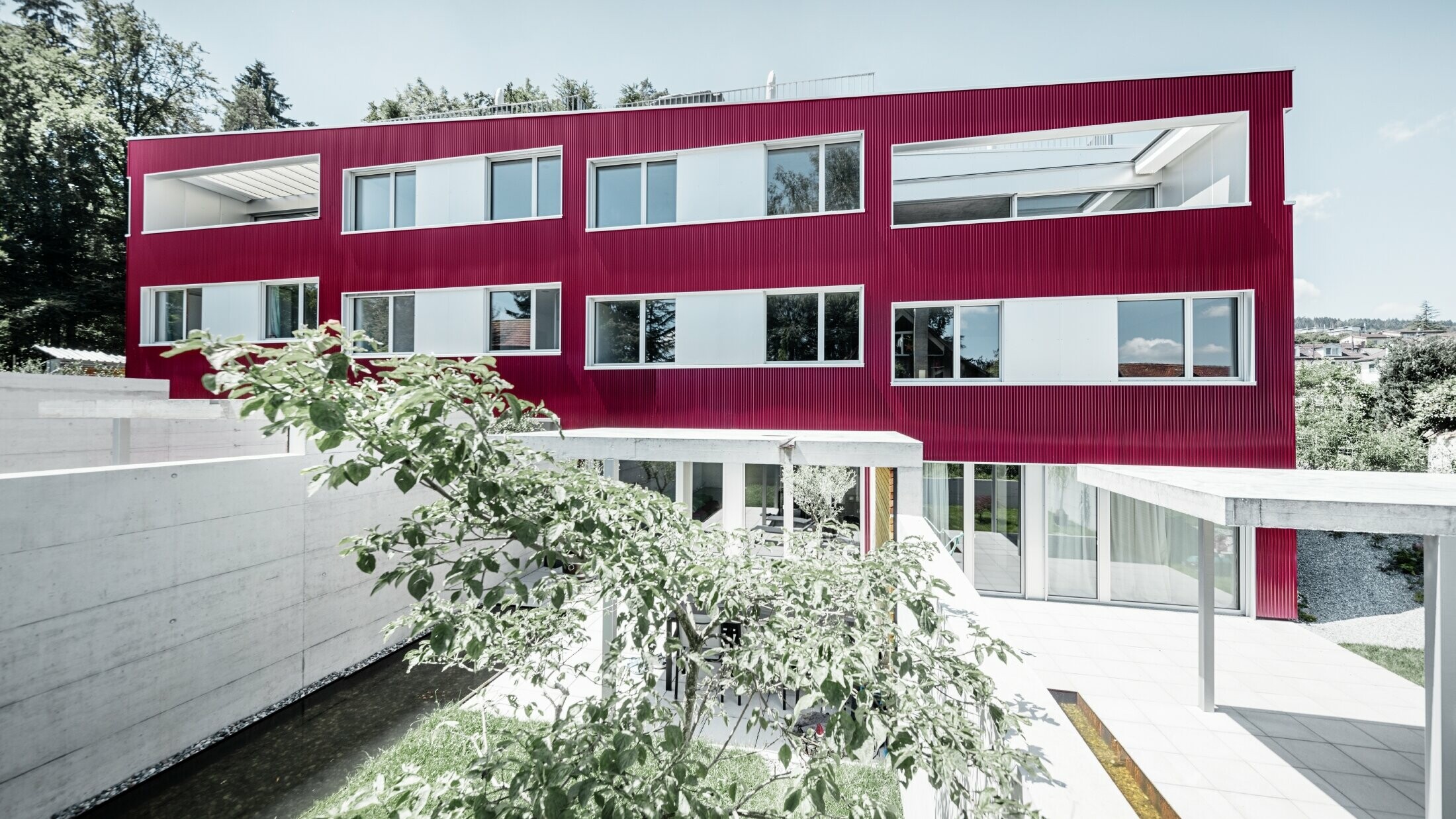 Bytový dom s plochou strechou a balkónmi s vínovočervenou fasádou s PREFA vlnitým profilom 