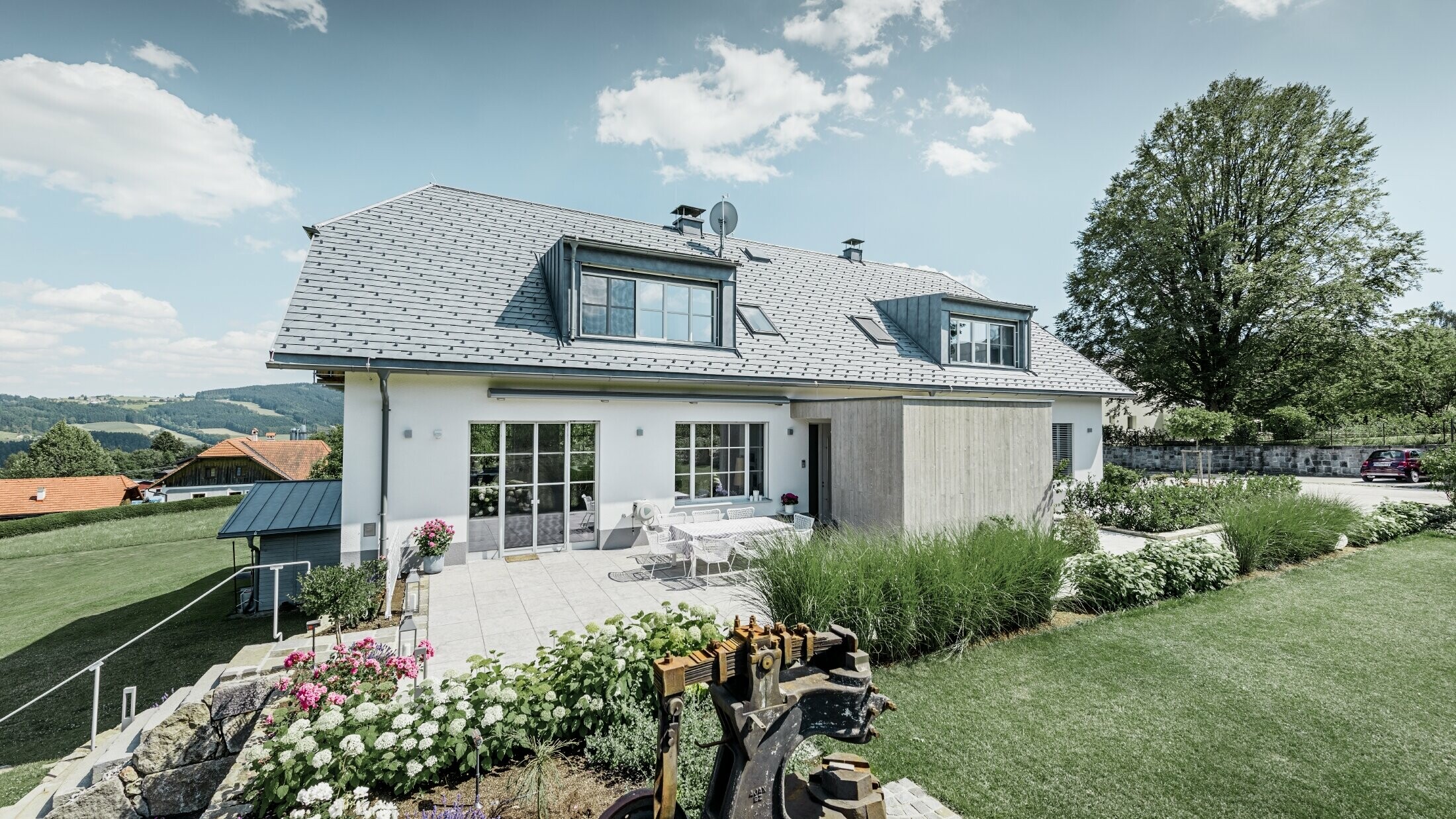 Klasický rodinný dom s polvalbovou strechou; dom so zrekonštruovanou strechou pokrytou strešným šindľom PREFA vo farbe kamenná šedá s krásne upravenou záhradou a veľkorysou terasou.