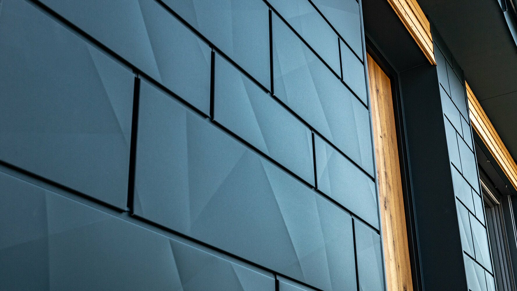 Fasádne panely PREFA s prelamovaným vzhľadom; hliníkový panel PREFA Siding.X v antracitovej farbe v kombinácii s drevenou fasádou.