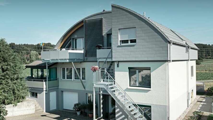 Obytný dom s valenou strechou pokrytou panelmi PREFA a Prefalz v svetlošedej farbe P.10