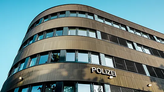 Dramatický pohľad zospodu na zakrivenú novú budovu policajného komisariátu č. 43 v Hamburgu: Výrazná hliníková fasáda PREFA z eloxovaných extrudovaných profilov „Zacke“ v odtieni strednej bronzy priťahuje ako architektonický magnet všetky pohľady. Jemná, rytmická štruktúra vytvára dynamické prechody svetla a tieňa a zdôrazňuje plynulé zaoblenia budovy. Hliník PREFA presviedča vysokou odolnosťou voči poveternostným vplyvom, ochranou proti korózii a dlhou životnosťou – ide o udržateľné riešenie s nízkymi nárokmi na údržbu pre precíznu, modernú fasádnu architektúru.