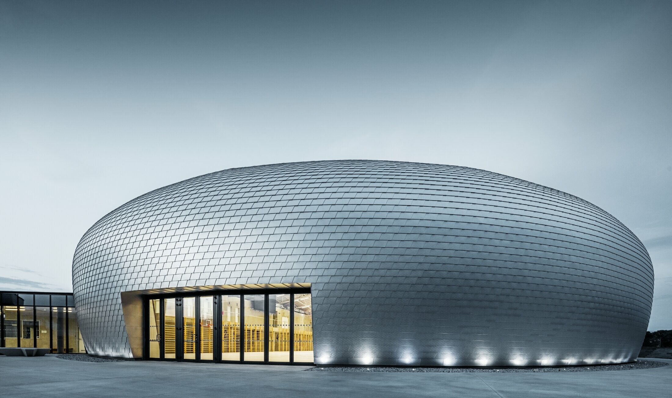 Sporthalle in Tschechien in Form eines UFOs verkleidet mit der PREFA Wandschindel in Naturblank bei Sonnenaufgang.