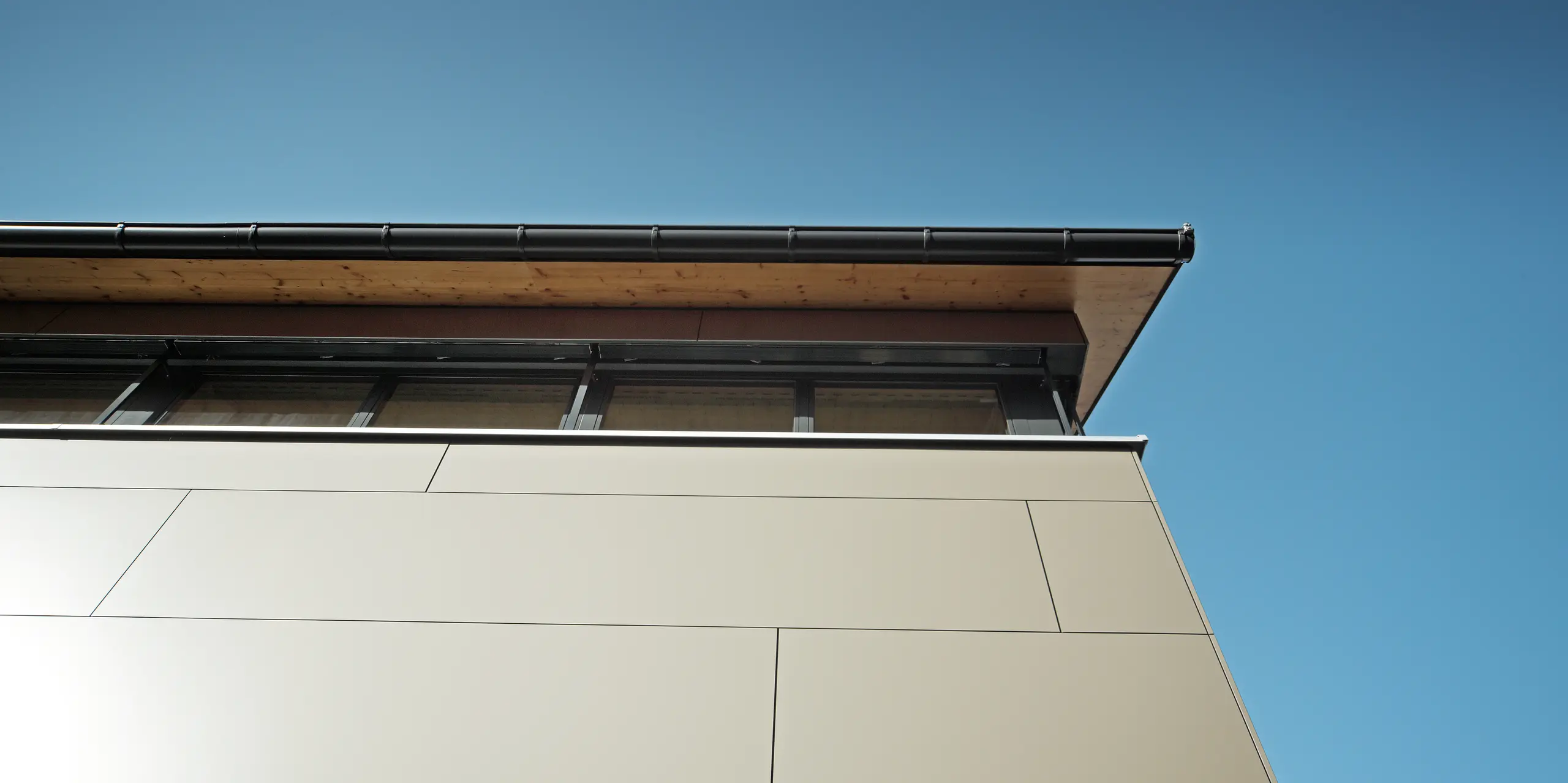 Detailný záber na fasádu rodinného domu v Hohenemse, ktorý je vybavený hliníkovými kompozitnými panelmi PREFA v bronzovej metalíze. Pri precíznej montáži nie sú viditeľné žiadne upevňovacie prvky, čo zdôrazňuje hladký a homogénny povrch. Vysokokvalitné panely odolné voči korózii poskytujú vďaka svojej robustnosti a farebnej stálosti dlhodobú ochranu a dodávajú domu moderný a jedinečný vzhľad.
