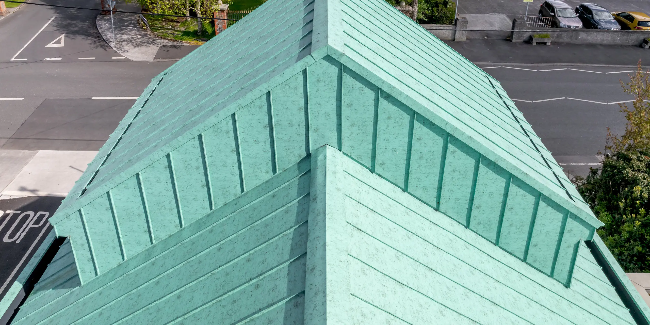 Nahaufnahme des markanten Giebelbereichs der St. Thomas Orthodox Church in Dublin mit PREFALZ Aluminium-Stehfalzdach in P.10 Patinagrün. Die Drohnenperspektive rückt die präzise ausgeführten Falzlinien, die klaren Dachkanten und das weithin sichtbare Kreuz auf dem First eindrucksvoll in den Mittelpunkt. Die lebendige Patinaoptik verleiht dem Dach eine edle, an historische Kupferdächer erinnernde Ausstrahlung und setzt einen starken architektonischen Akzent im Stadtbild. Das hochwertige PREFA Aluminium überzeugt durch Korrosionsbeständigkeit, Langlebigkeit, geringes Gewicht und hohe Farbbrillanz und bietet damit eine nachhaltige Dachlösung für anspruchsvolle Sakralarchitektur.