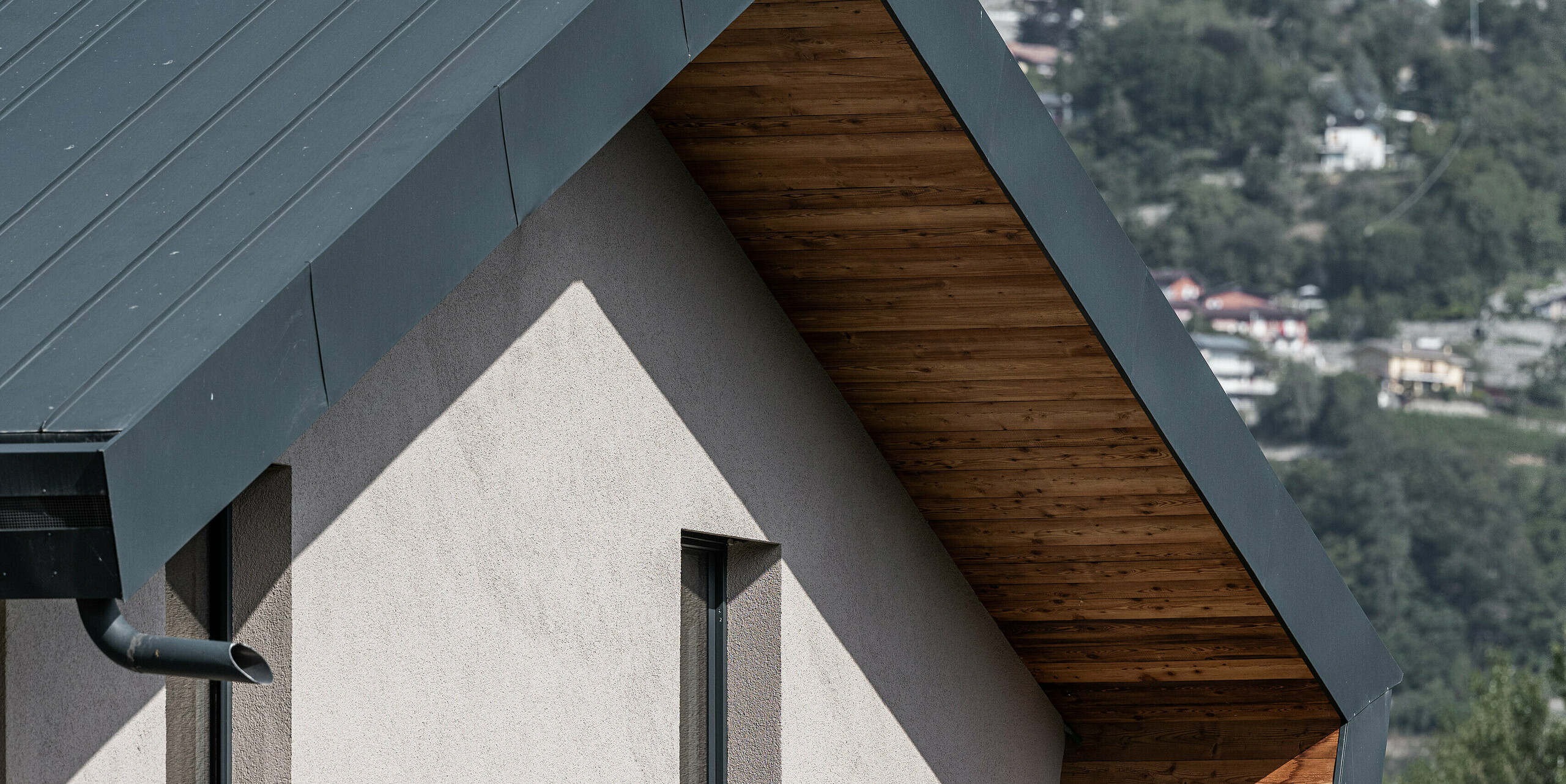Detailný pohľad na vilu Tia v Taliansku, vybavenú kompletným systémom PREFA. Pohľad zobrazuje hliníkový obklad PREFALZ vo farbe P.10 antracitová, ktorý elegantne zvýrazňuje teplé drevené podkonštrukcie. Precízne spracovanie a moderný dizajn odrážajú kvalitu hliníkových výrobkov PREFA, ktoré sú známe svojou odolnosťou a estetikou.