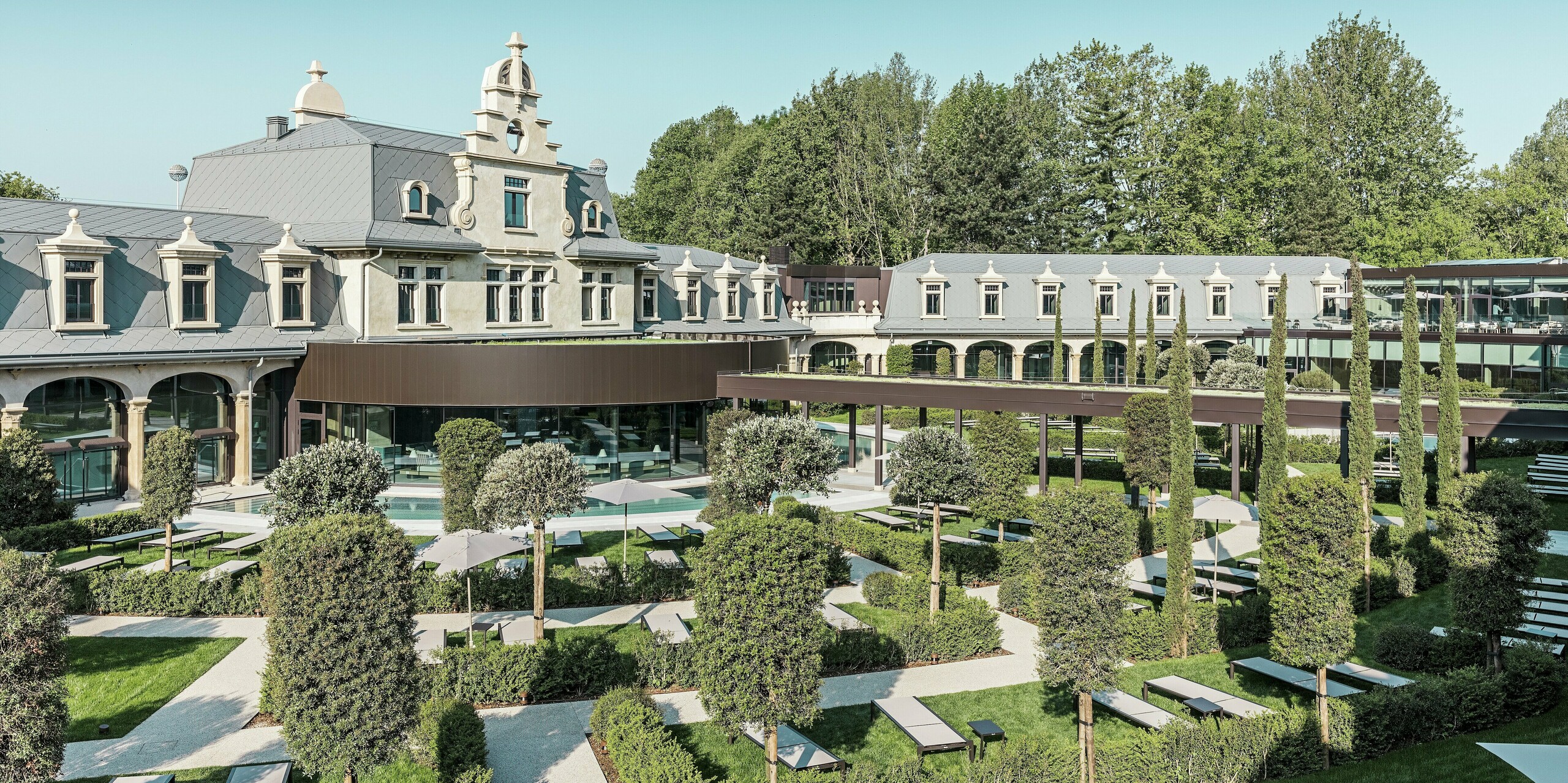 Starostlivo zrekonštruovaný termálny park „De Montel – Terme Milano“ disponuje modernou záhradnou krajinou s rovnými chodníkmi, oddychovými zónami a stredomorskou vegetáciou. Štýlová strešná krytina PREFA šablóna 44 × 44 v odtieni P.10 svetlošedá zdôrazňuje historickú architektúru, zatiaľ čo moderné sklenené prvky a zelený prístrešok vytvárajú prepojenie s súčasným využitím.