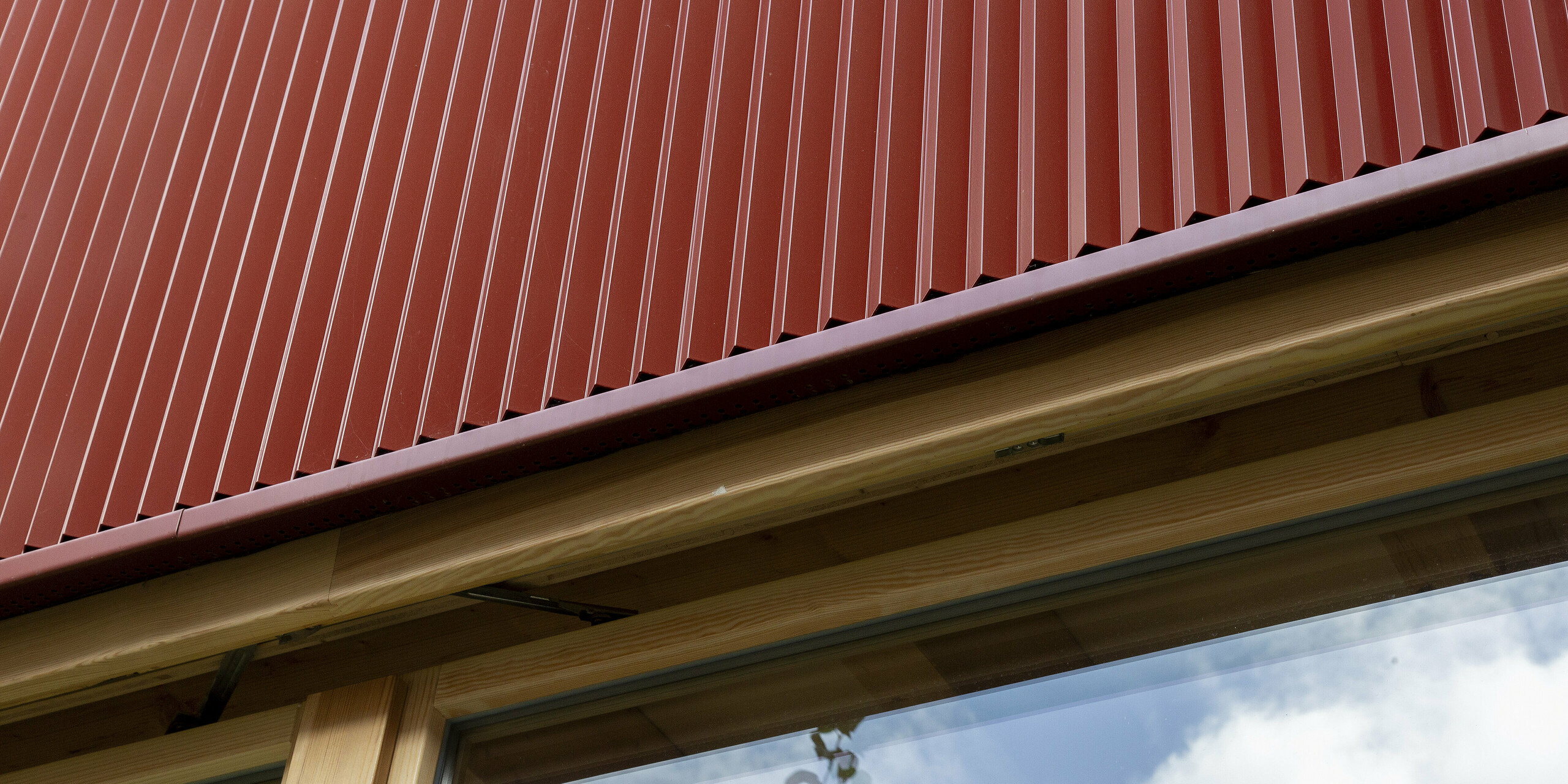 Die glatten Linien des PREFA Zackenprofils in der Farbe Oxydrot dominieren die klare Fassadenansicht. Die vertikale Riffelung erzeugt ein kraftvolles Lichtspiel, das das moderne Design hervorhebt. In Kombination mit der warmen Holzoptik und den großzügigen Glasflächen ergibt sich ein langlebiges und stilvolles Gestaltungskonzept.
