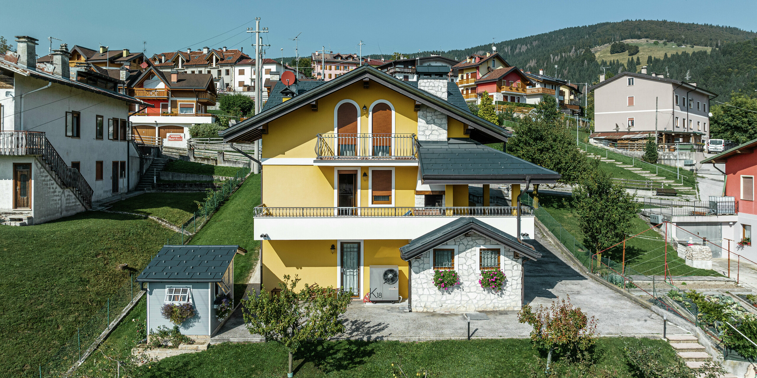 Rodinný dom v Gallio s alpským šarmom a modernou hliníkovou strechou PREFA v tmavošedej farbe P.10. Odolné strešné panely PREFA R.16 zaisťujú optimálnu ochranu pred poveternostnými vplyvmi a atraktívny vzhľad. Žltá fasáda na zadnej strane budovy bola kombinovaná s prvkami z prírodného kameňa a drevenými akcentmi – dokonalá symbióza so zeleným okolím. Vysoko kvalitnú plechovú strechu dopĺňa odvodňovací systém PREFA, ktorý zaisťuje spoľahlivé odvádzanie vody. Elegantný strešný systém, ktorý spája funkčnosť a estetiku.