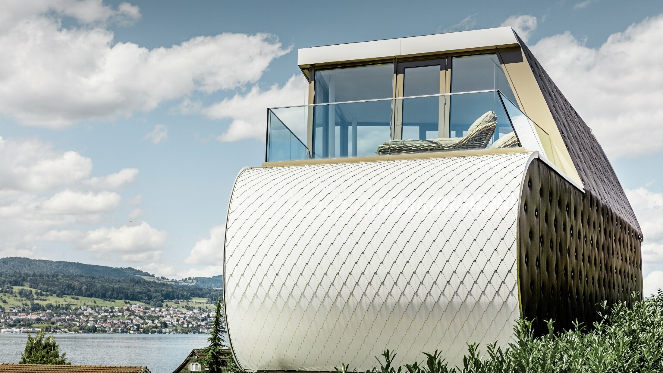 Bočný pohľad na ocenený Flexhouse, navrhnutý architektom Camenzind; je vidno jednu zo zakrivených vonkajších stien, ktoré sú obložené so šupinatou hliníkovou fasádou od PREFA vo farbe čistá biela.