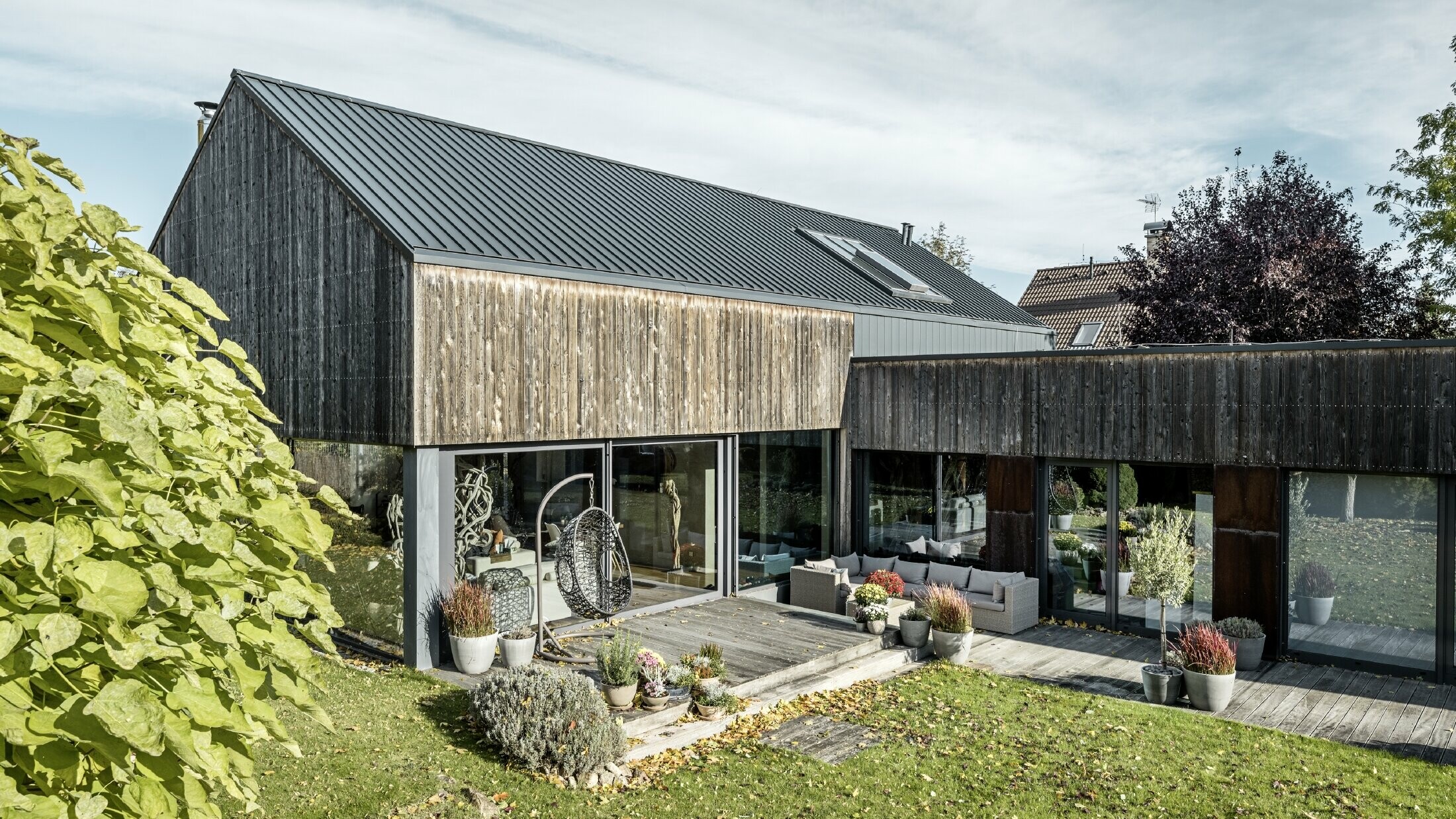 Rodinný dom so sedlovou strechou, zakrytou s dvojitou stojatou drážkou PREFALZ vo farebnom vyhotovení antracitová a zvetranou drevenou fasádou. S peknou drevenou terasou a veľkými okennými plochami na prízemí.