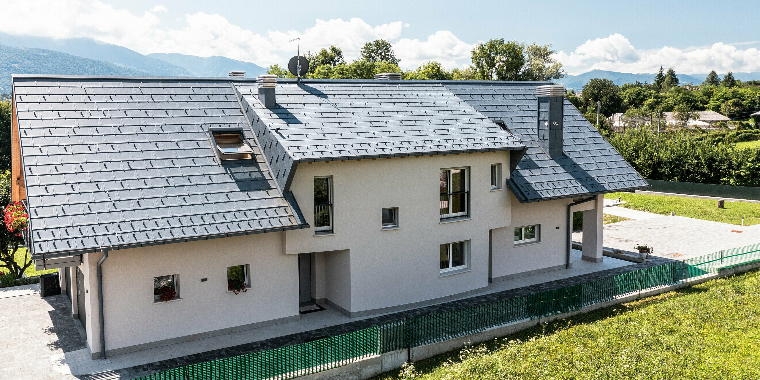 Rodinný dom v talianskom Belluno s elegantnou strechou PREFA zo strešných panelov R.16 vo farbe P.10 antracitová. Systém odvodnenia strechy pozostávajúci z hranatého žľabu a odvodňovacej rúry je farebne zladený a dotvára estetický a funkčný dizajn strechy. Svojou tradičnou konštrukciou a moderným strešným materiálom tvorí dom atraktívny kontrast k malebnej horskej kulisy.