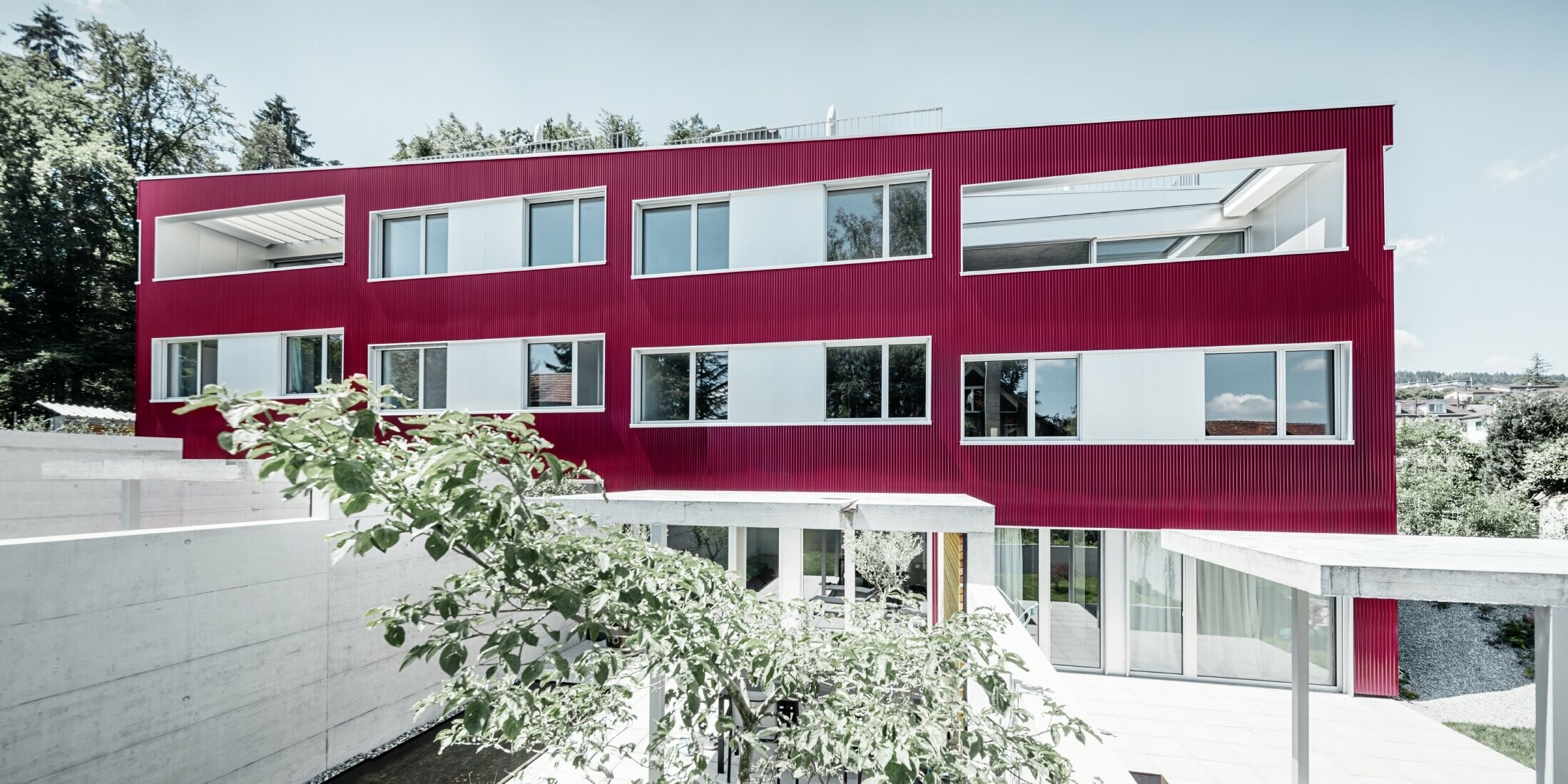Bytový dom s plochou strechou a balkónmi s vínovočervenou fasádou s PREFA vlnitým profilom 