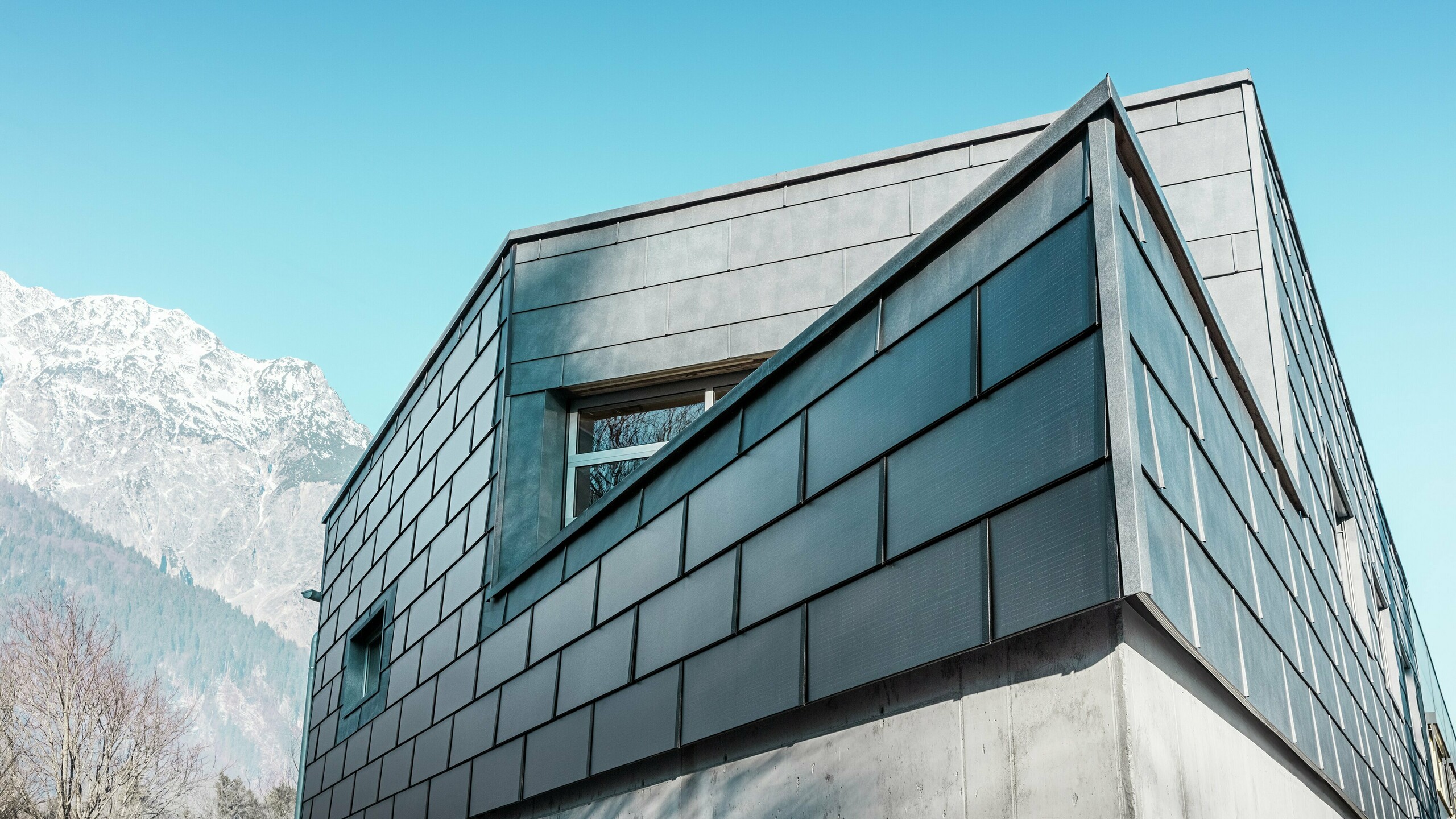 Moderná fasáda budovy s integrovanými solárnymi panelmi PREFA: Udržateľné hliníkové panely s integrovanou fotovoltikou vyrábajú elektrickú energiu a harmonicky zapadajú do architektonického dizajnu.