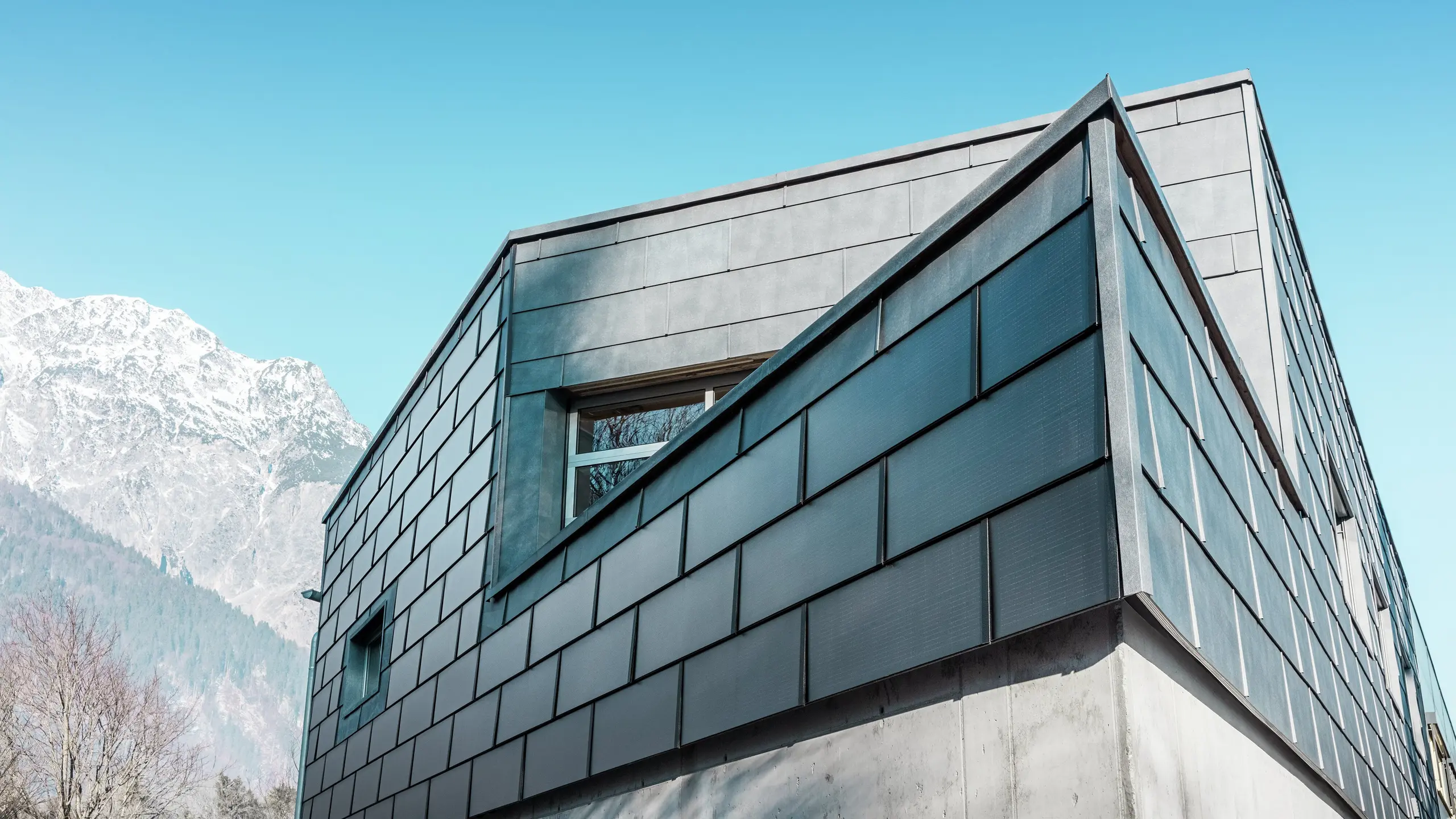 Moderná fasáda budovy s integrovanými solárnymi panelmi PREFA: Udržateľné hliníkové panely s integrovanou fotovoltikou vyrábajú elektrickú energiu a harmonicky zapadajú do architektonického dizajnu.