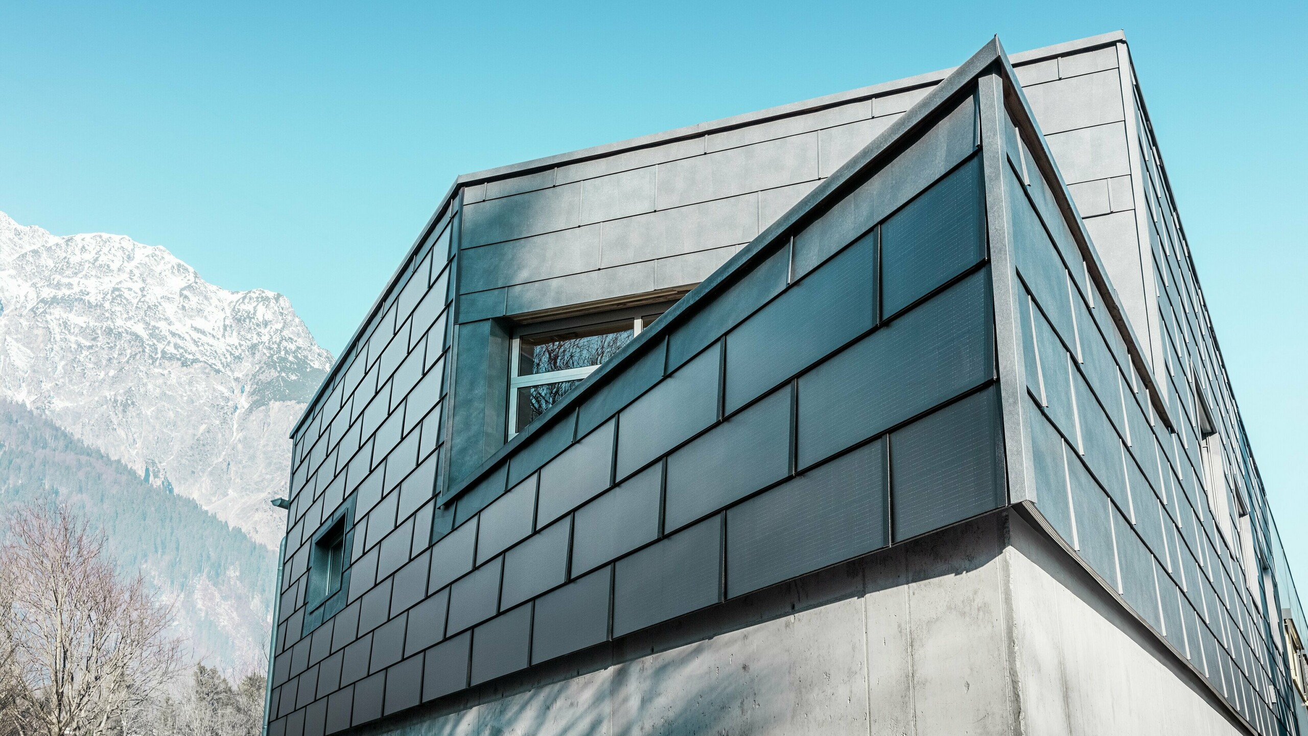Moderná fasáda budovy s integrovanými solárnymi panelmi PREFA: Udržateľné hliníkové panely s integrovanou fotovoltikou vyrábajú elektrickú energiu a harmonicky zapadajú do architektonického dizajnu.