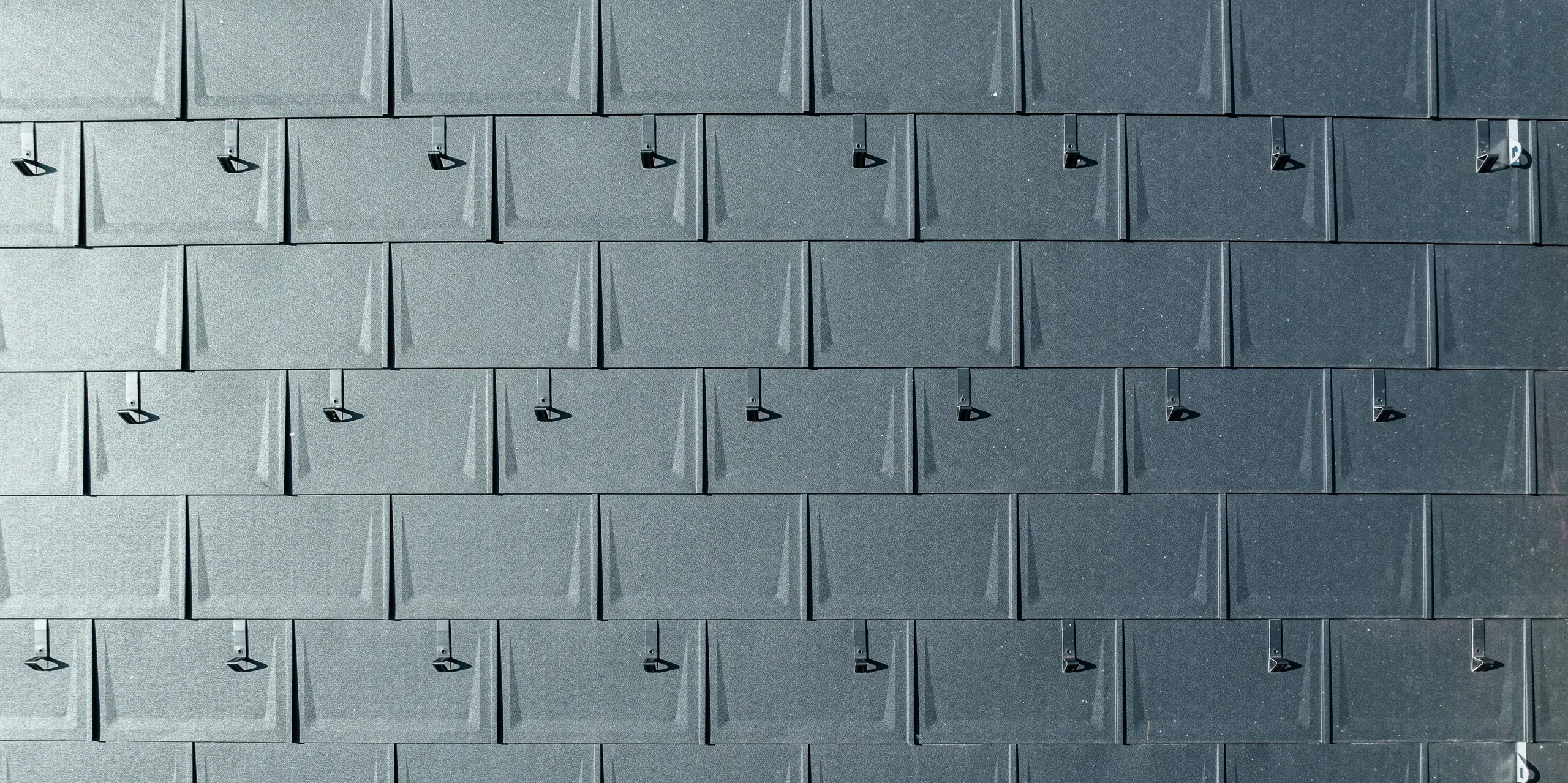 Detailný záber hliníkovej strešnej krytiny PREFA. Strešné panely PREFA R.16 v obľúbenej farbe P.10 antracit sú presne spojené. Vysokokvalitné hliníkové panely ponúkajú odolné, poveternostným vplyvom odolné a vizuálne príťažlivé strešné riešenie. Snehové zábrany poskytujú dodatočnú bezpečnosť.