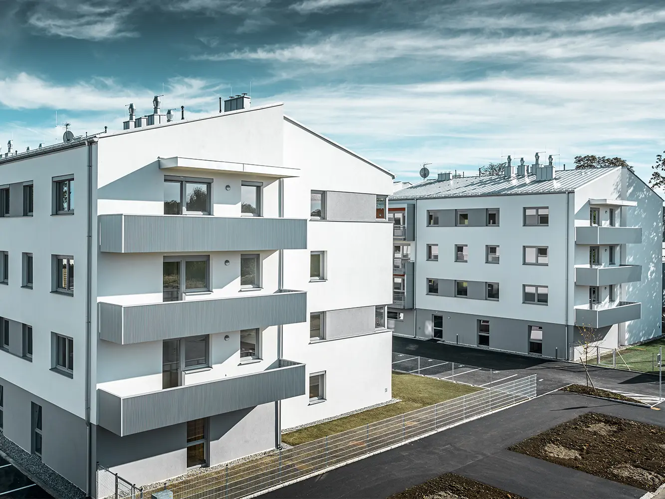 Moderný bytový komplex s bielou fasádou a balkónmi s PREFA prelamovaným profilom v odtieni strieborná metalíza