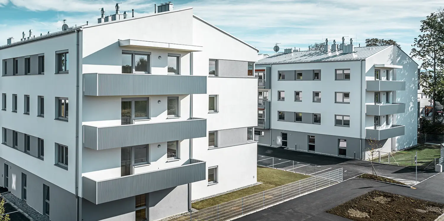 Moderný bytový komplex s bielou fasádou a balkónmi s PREFA prelamovaným profilom v odtieni strieborná metalíza