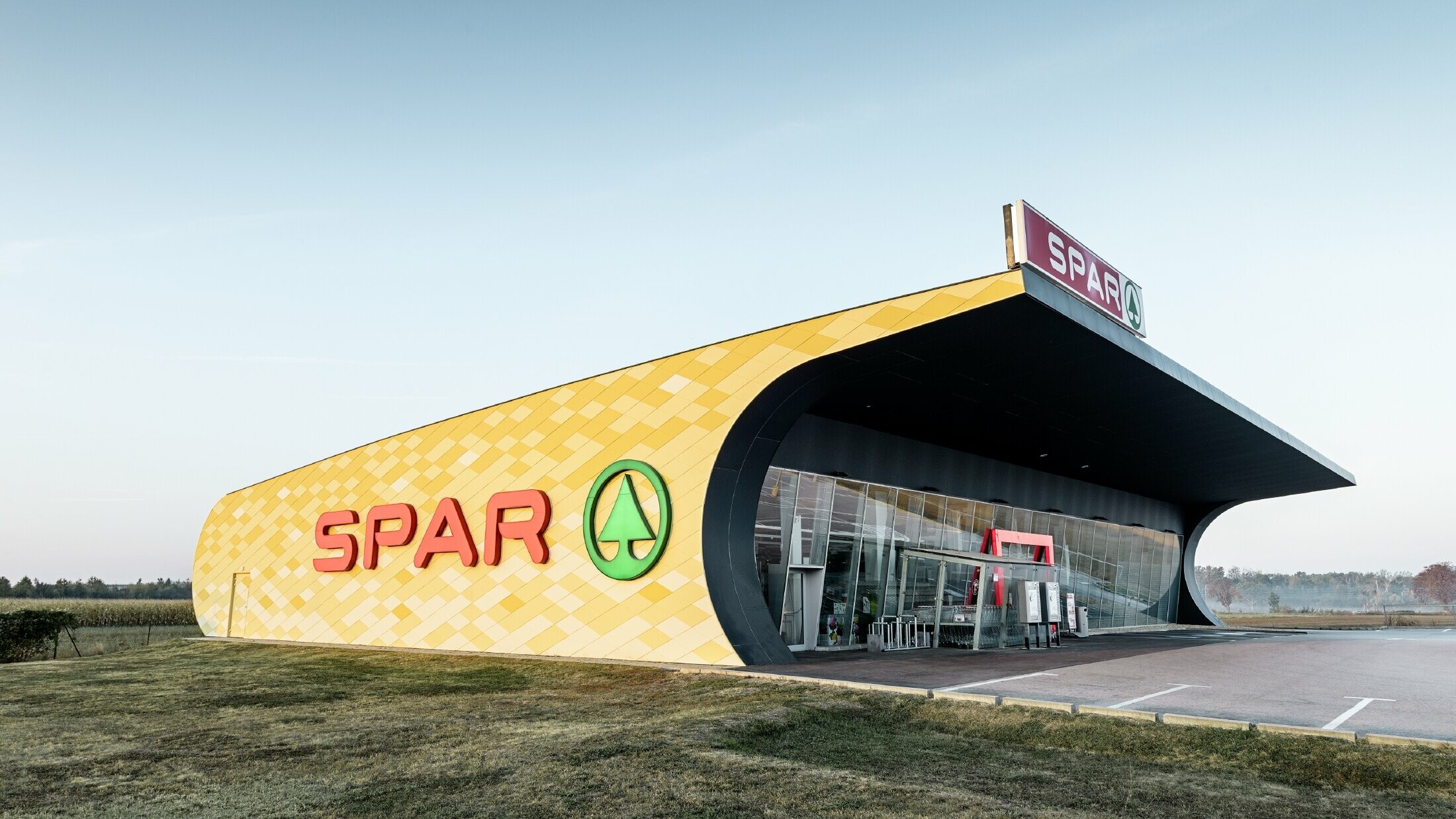 Predajňa obchodného reťazca Spar s hliníkovou fasádou v žltooranžovom károvanom dizajne s logom Spar