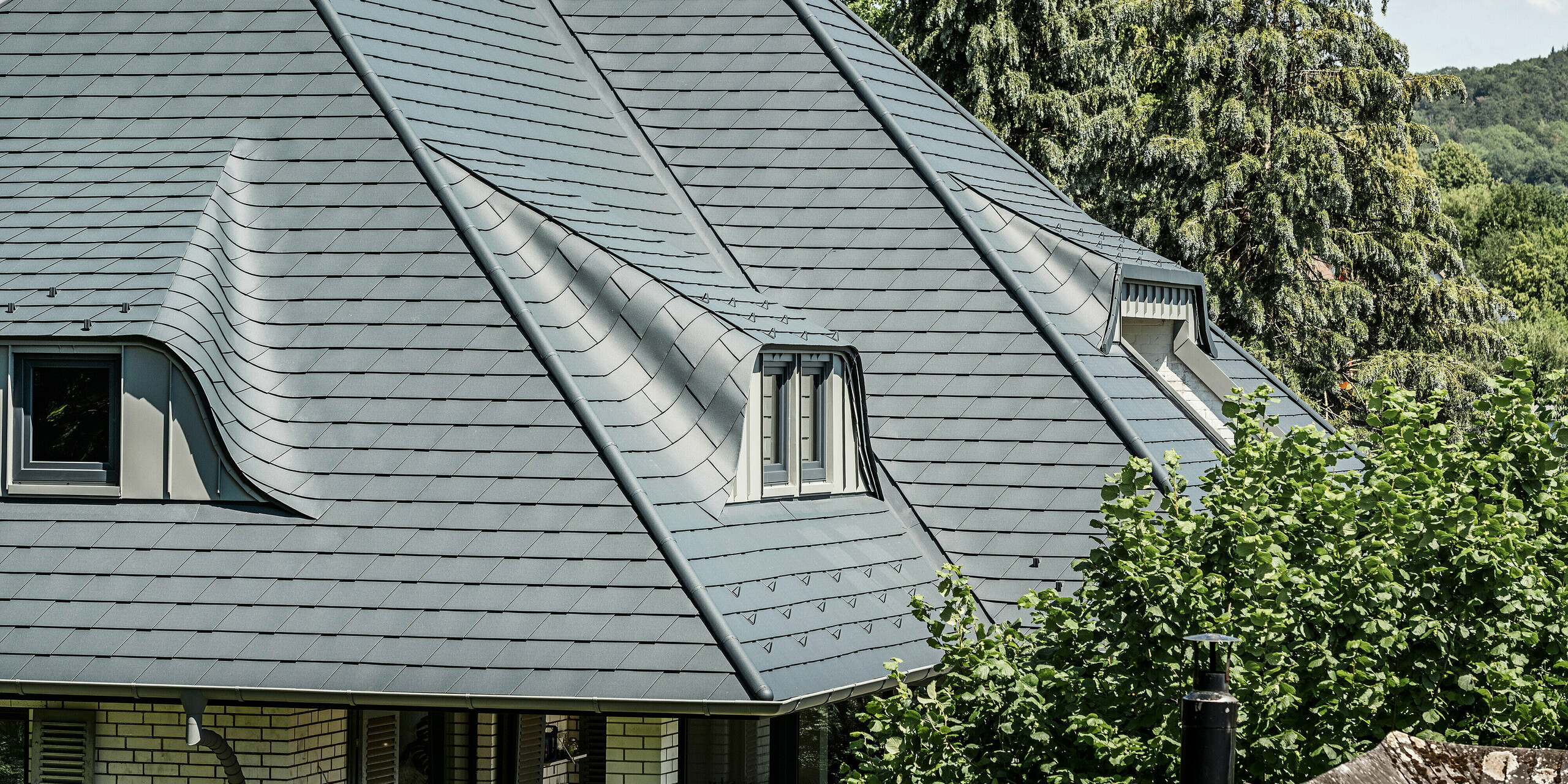 Strecha so zakrivenými vikiermi na rodinnom dome v Einbecku pokrytá strešnými šindľami PREFA v antracitovej farbe P.10