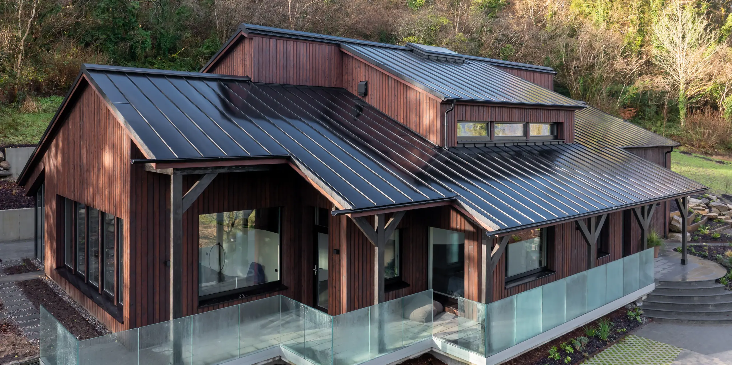 Schrägansicht auf das House of Holywell in Sligo: Die Perspektive führt entlang der geneigten Dachflächen, auf denen das PREFALZ Aluminiumdach in P.10 Schwarz seine präzise Stehfalzstruktur eindrucksvoll entfaltet. Die klaren Linien verlaufen dynamisch über mehrere Ebenen und lenken den Blick zur erhöhten Dachzone mit Gaube. Die leicht spiegelnde Oberfläche betont die hochwertige Verarbeitung und sorgt für eine elegante Tiefenwirkung. PREFA Aluminium überzeugt dabei durch Langlebigkeit, Korrosionsbeständigkeit und zuverlässigen Schutz in anspruchsvollem Klima.