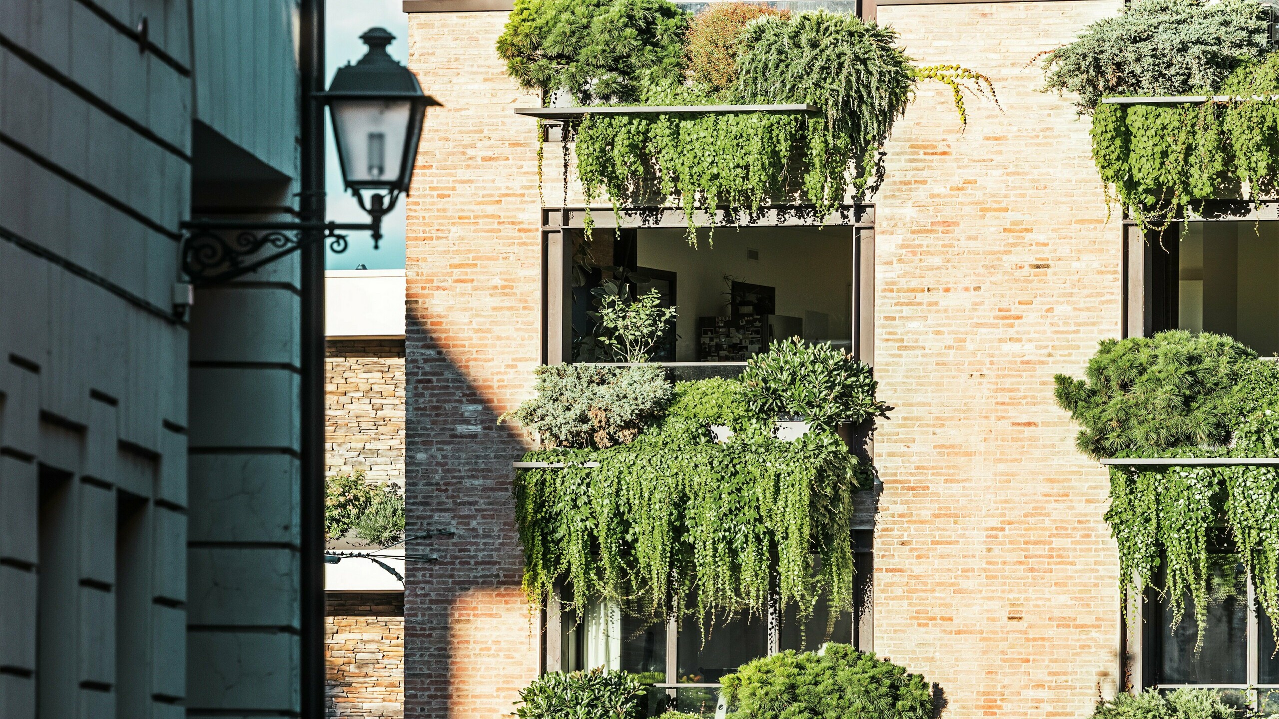 Detailný pohľad na zelenú tehlovú fasádu v Taliansku so závesnými záhradami, architektonickými detailmi PREFALZ a priľahlým prostredím starého mesta s laternou.