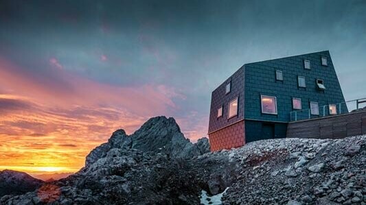Výnimočná architektúra v horách: chata Seethalerhütte na Dachsteine pokrytá strešným a fasádnym panelom PREFA FX.12 v odtieni kamenná šedá.