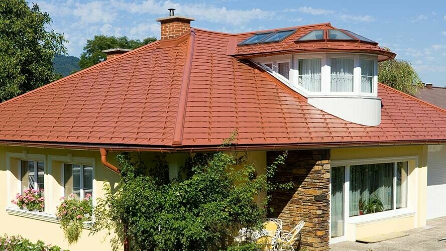 Rodinný dom s valbovou strechou a vikierom zastrešený hliníkovým šindľom PREFA vo vzhľade škridly v tehlovočervenej farbe.