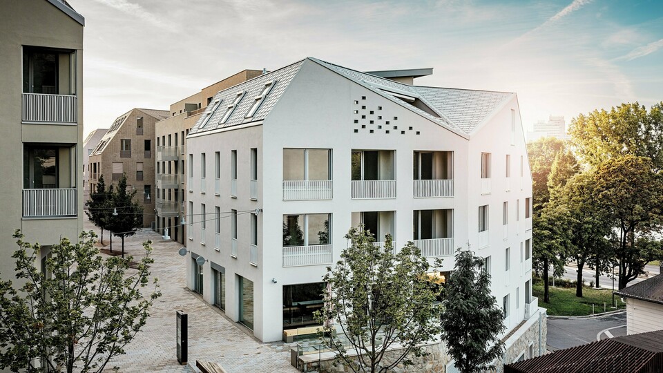 Moderná obytná štvrť Vydrica v Bratislave sa vyznačuje jasným architektonickým jazykom a pokojnou atmosférou uličiek. Strmé sedlové strechy s výraznými strešnými oknami sú pokryté hliníkovými strešnými šindľami PREFA vo farbách P.10 prefa biela, bronzová a P.10 pieskovo hnedá, ktoré na slnku vytvárajú elegantný vizuálny akcent. Precízne vyhotovené línie a homogénne plochy podčiarkujú vysokú kvalitu architektonického riešenia. Hliník PREFA presviedča dlhou životnosťou, nízkou hmotnosťou a vysokou odolnosťou voči poveternostným vplyvom – ideálne riešenie pre zložité tvary striech a udržateľný, nenáročný obvodový plášť budovy.