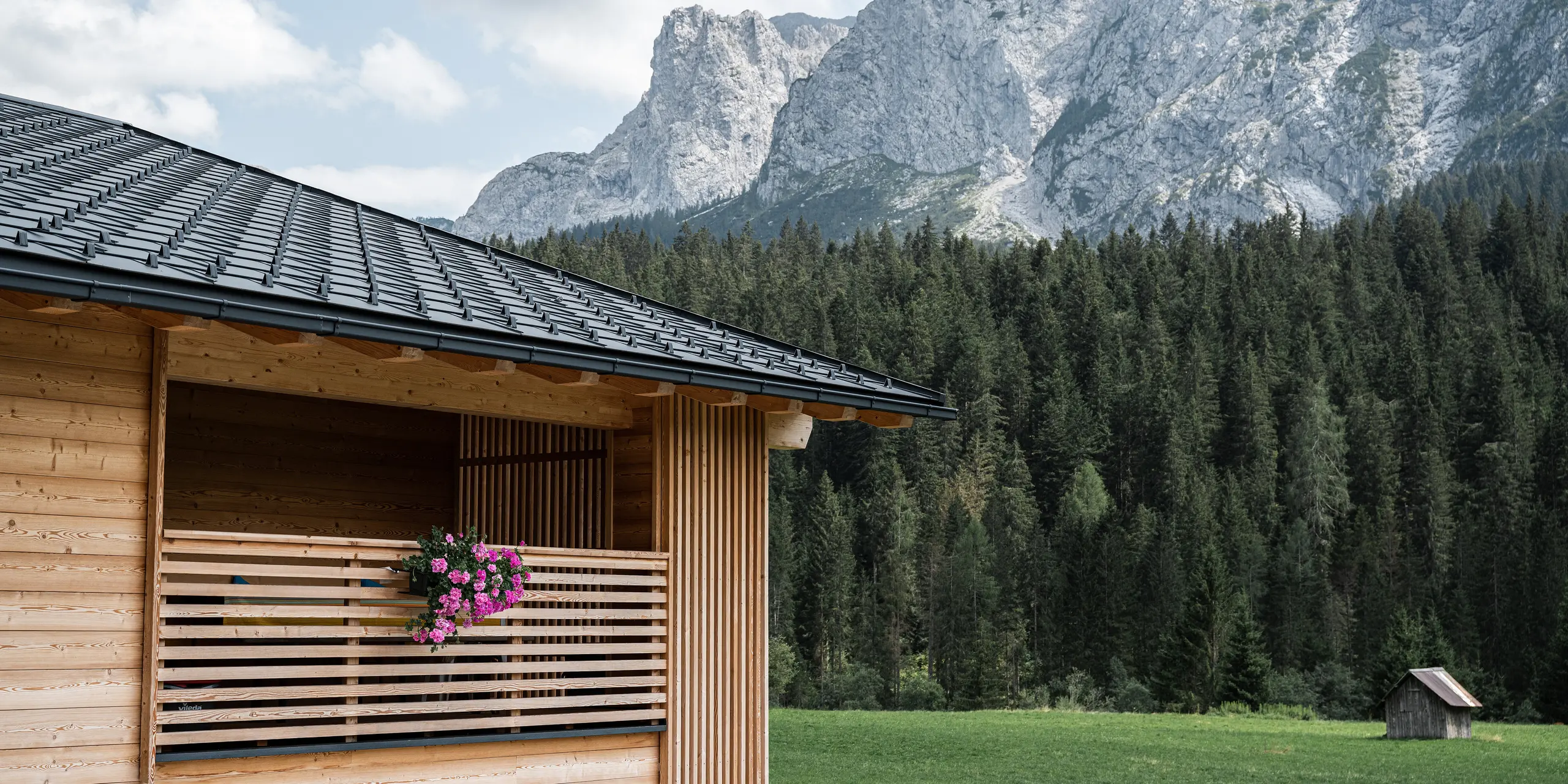 Casa Hope v Sappade v severnom Taliansku, zapustená v Dolomitoch, so strechou PREFA zo strešných panelov R.16 v čiernej farbe P.10. Čisté línie strechy kontrastujú s prírodnou drevenou fasádou a loggiou, ktorú zdobia kvitnúce rastliny. Tento obraz spája modernú stavebnú technológiu s tradičnou alpskou kultúrou bývania, obklopenú pôsobivou prírodou.