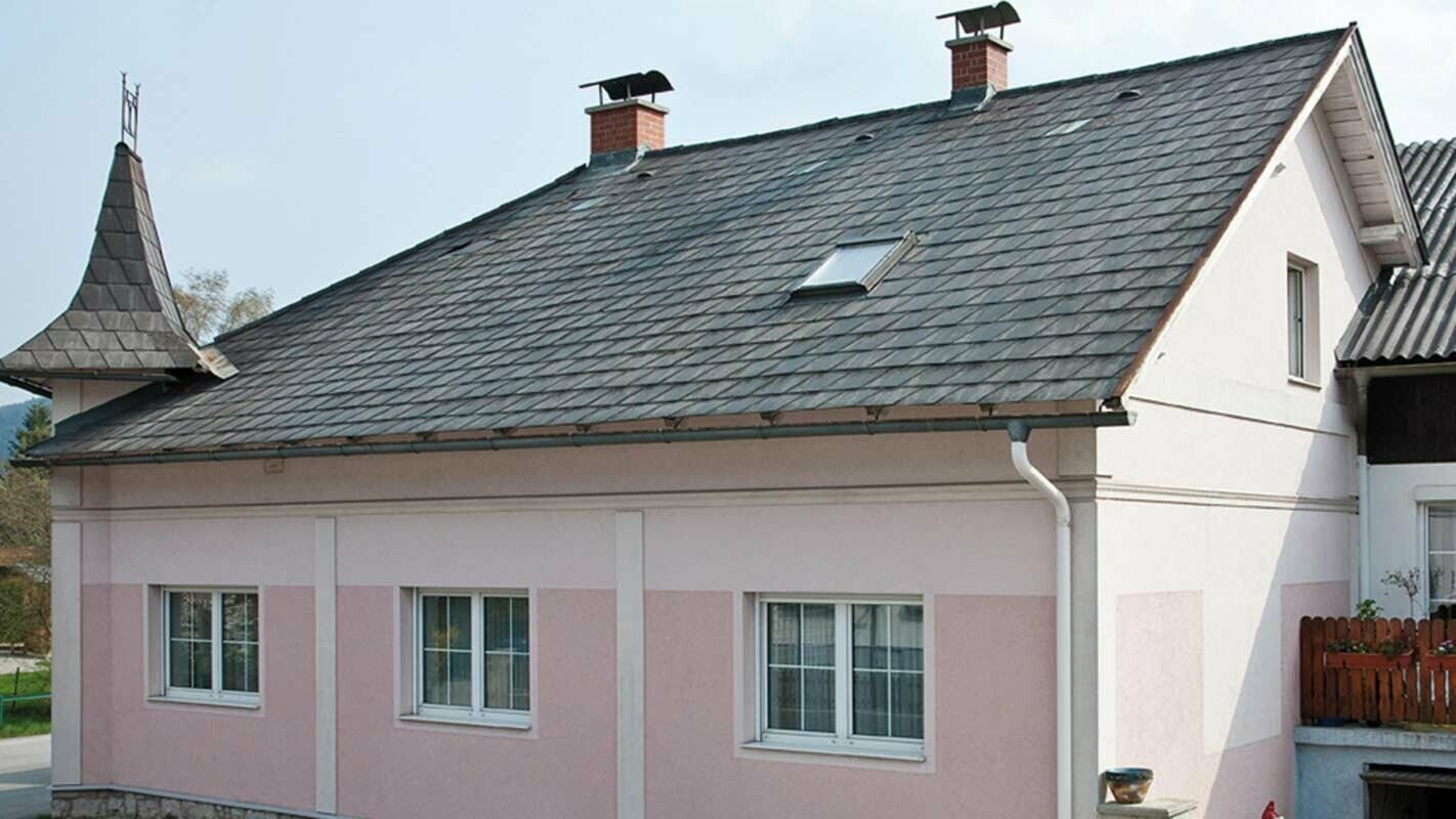 Dom v Rakúsku s vežičkami a ružovou fasádou pred rekonštrukciou strechy s použitím PREFA falcovaných škridiel - pôvodne vláknocementová krytina Eternit