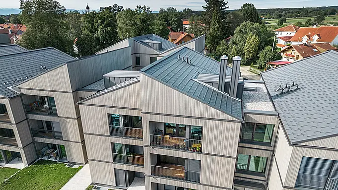Moderný bytový dom v meste Utting am Ammersee, ktorý sa vyznačuje inovatívnou hybridnou konštrukciou s elegantnou drevenou fasádou a vysokokvalitným hliníkovým strešným systémom PREFA. Boli použité tmavosivé strešné panely R.16 a PREFALZ. Budova zaujme jasnými líniami, udržateľnými materiálmi a harmonickým začlenením do zeleného okolia. Architektonický návrh spája estetiku a funkčnosť, pričom trvanlivé výrobky PREFA odolné voči poveternostným vplyvom výrazne prispievajú k vysokej kvalite a pôsobivému vzhľadu.