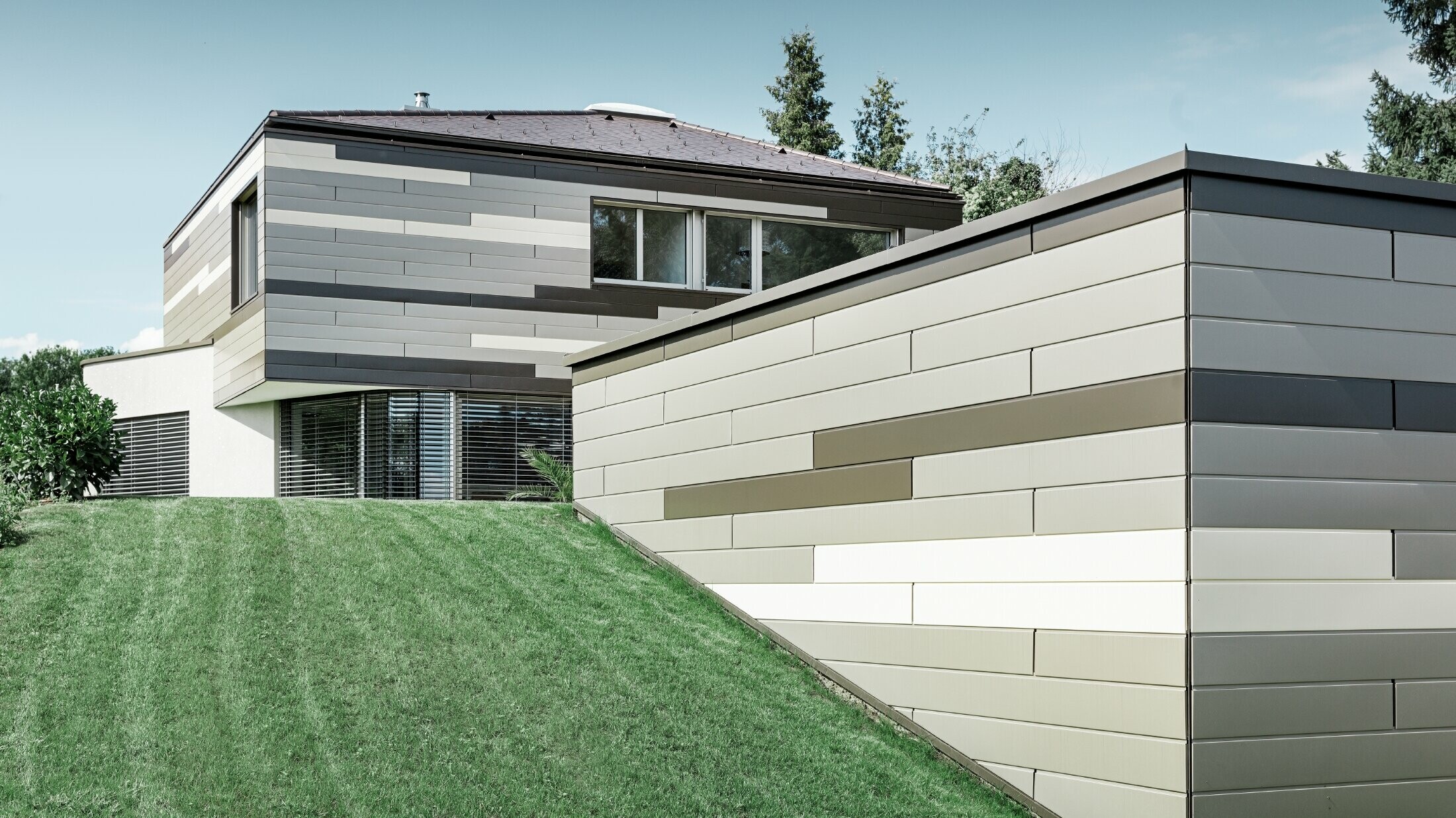 Moderný rodinný dom s plochou strechou a krytou terasou s individuálne navrhnutou hliníkovou fasádou PREFA vo farbách hnedá, bronzová a slonová kosť