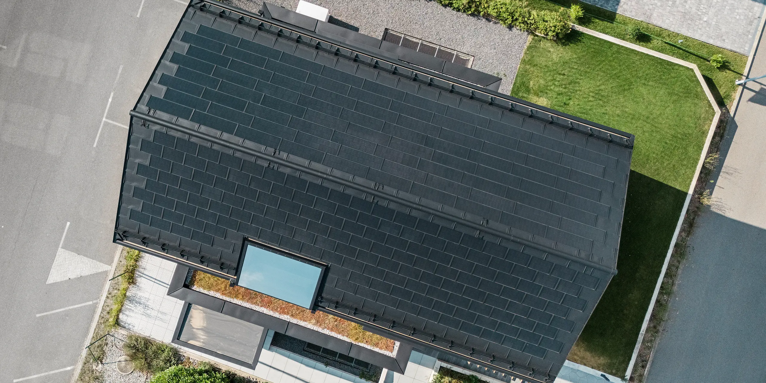 Pohľad z vtáčej perspektívy na modelový dom Autark v centre montovaných domov Blaue Lagune, Vösendorf (AT). Strecha je pokrytá integrovanými solárnymi panelmi PREFA a strešnými panelmi R.16 s vysokokvalitným náterom P.10. Inovatívny strešný systém s integrovanými fotovoltickými modulmi zaisťuje pôsobivý vzhľad a trvalo udržateľnú výrobu energie zo slnečnej energie.
