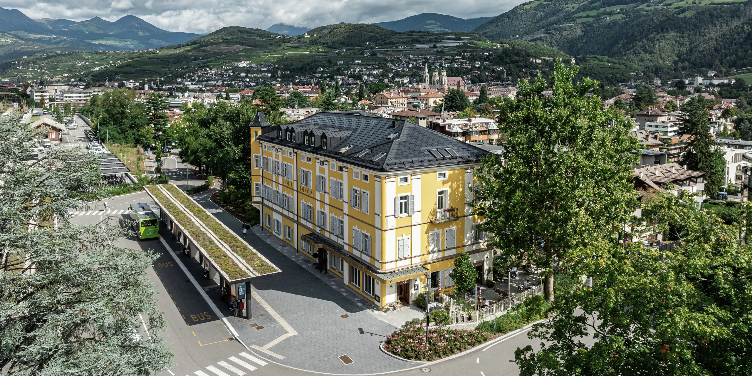 Panoramatický pohľad na hotel Jarolim v Brixene, vybavený modernou strechou PREFA z integrovaných solárnych panelov a strešných panelov R.16. Poveternostne odolná hliníková strecha spája udržateľnú výrobu energie s elegantnou estetikou a harmonicky zapadá do pamiatkovo chránenej architektúry budovy. Obklopený malebnou juhotirolskou krajinou, hotel ukazuje, ako sa dá dokonale spojiť tradícia a inovácie.