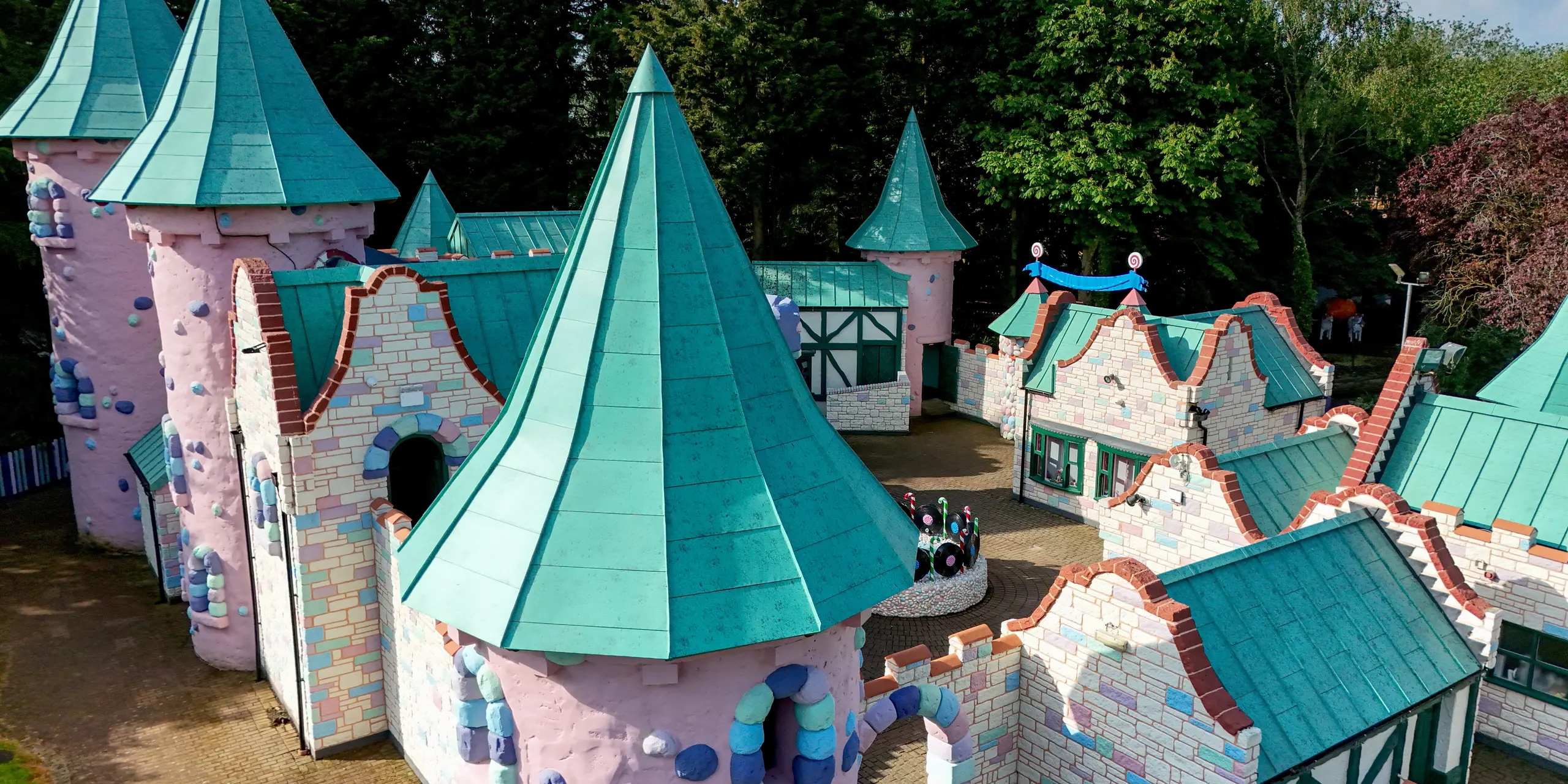 Detailreiche Ansicht einer verspielten Schlosslandschaft im Sundown Adventureland mit markanten, konischen Türmen als visuelle Eyecatcher. Die PREFALZ Aluminiumdächer in P.10 Patinagrün prägen das Erscheinungsbild und heben die geschwungenen Formen sowie die komplexen Dachgeometrien eindrucksvoll hervor. Präzise Stehfalze unterstreichen die hochwertige Verarbeitung. Gleichzeitig überzeugen die PREFA Dächer durch extreme Langlebigkeit, Korrosionsbeständigkeit und zuverlässige Widerstandsfähigkeit gegenüber unterschiedlichsten Witterungseinflüssen.