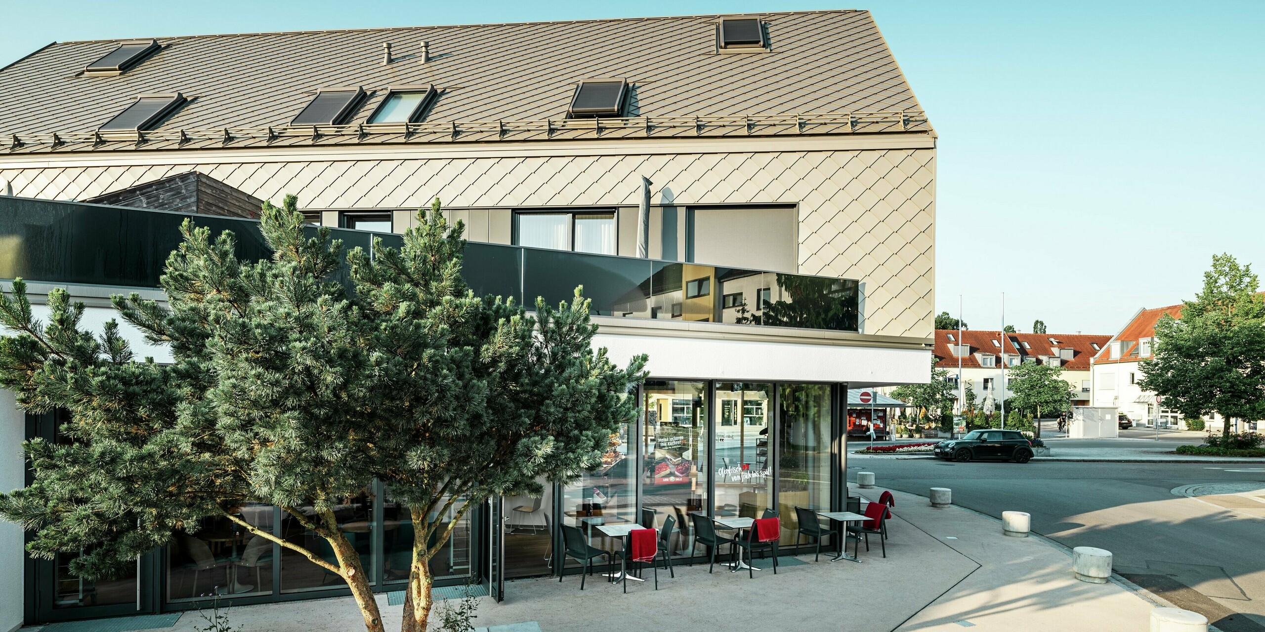 Moderný bytový dom s výrazným dizajnom fasády v Leitershofene, Nemecko. Budova je obložená odolnými strešnými a fasádnymi šablónami PREFA 29 × 29 vo farbe bronzová, ktoré vytvárajú štýlový a nadčasový vzhľad. Kombinácia jasných línií, veľkých okien a svetlej omietnutej fasády na prízemí podčiarkuje kvalitnú architektúru. Hliníkové strešné a fasádne prvky ponúkajú okrem estetickej elegancie aj vysokú odolnosť voči poveternostným vplyvom a trvanlivosť.