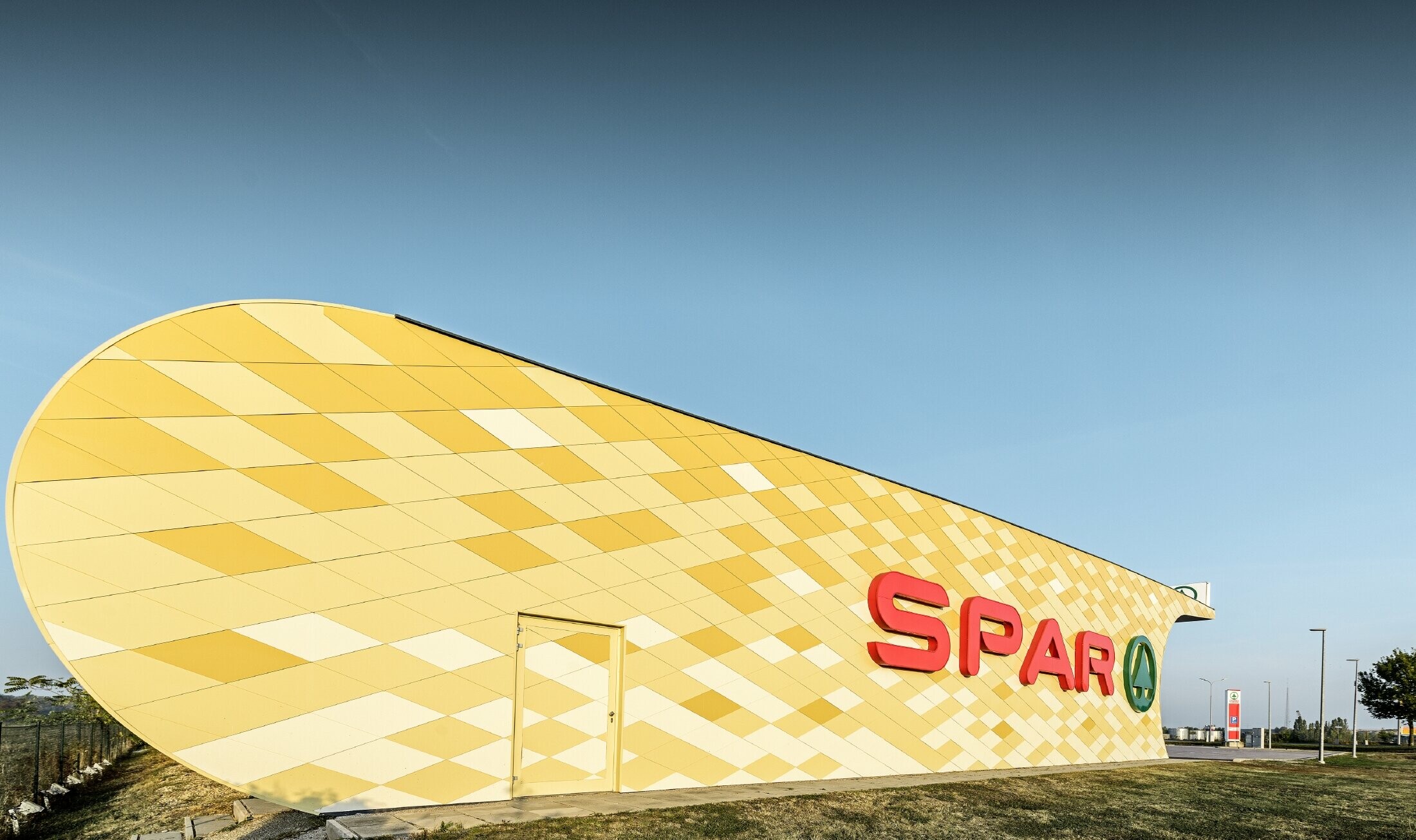 Predajňa obchodného reťazca Spar s hliníkovou fasádou v žltooranžovom károvanom dizajne s logom Spar