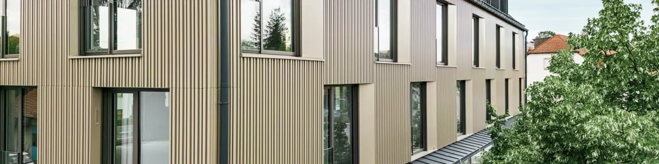 Na snímke je moderná budova vo Feldkirchene, ktorú navrhol architekt Stefan Heigl. Fasáda je z materiálu Prefalz vo farbe bronzová a šikmá strecha je pokrytá materiálom Prefalz v čiernošedej farbe. Veľké okná poskytujú vo vnútri dostatok svetla, zatiaľ čo presklená zóna na prízemí ponúka príjemný priestor na stravovanie. Kvalitný výber materiálov a elegantný dizajn dodávajú budove moderný a štýlový vzhľad.