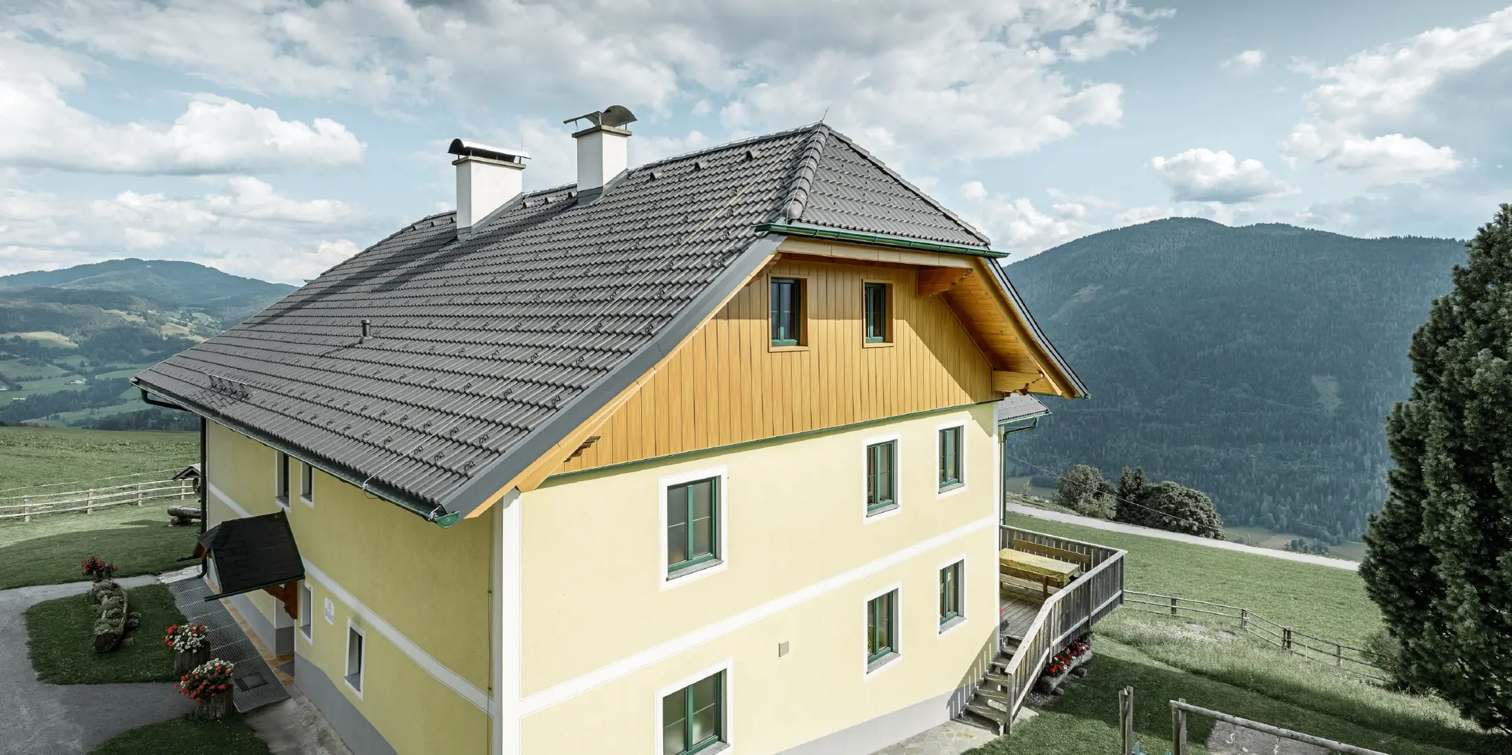 Giebelverkleidung aus witterungsbeständigem Aluminium: Ein mehrstöckiges Wohnhaus in Ranten wurde an der Giebelseite mit PREFA Sidings in Holzoptik verkleidet. Das traditionelle Wohnhaus liegt idyllisch mit Blick auf die Berge und einem kleinen Kinderspielplatz im Garten.
