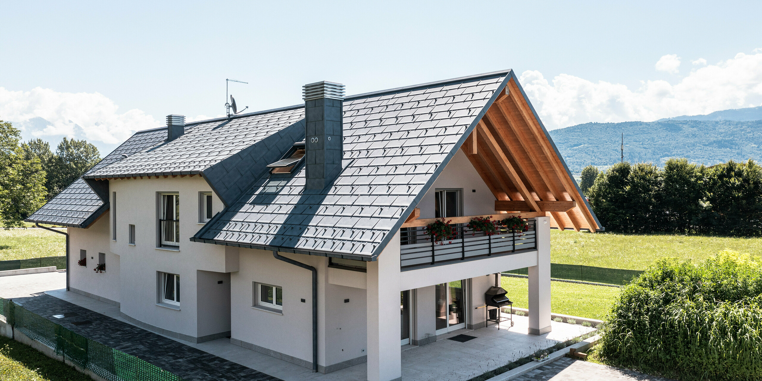 Očarujúci rodinný dom v Bellune v severnom Taliansku korunovaný strešným panelom PREFA R.16 v antracitovej farbe. Strecha s povrchom P.10 odráža robustnú eleganciu a technickú vyspelosť, ktoré charakterizujú produkty PREFA. Farba je v súlade so sviežimi zelenými lúkami a horskou panorámou v pozadí. Na obrázku je terasa s loggiou hore.