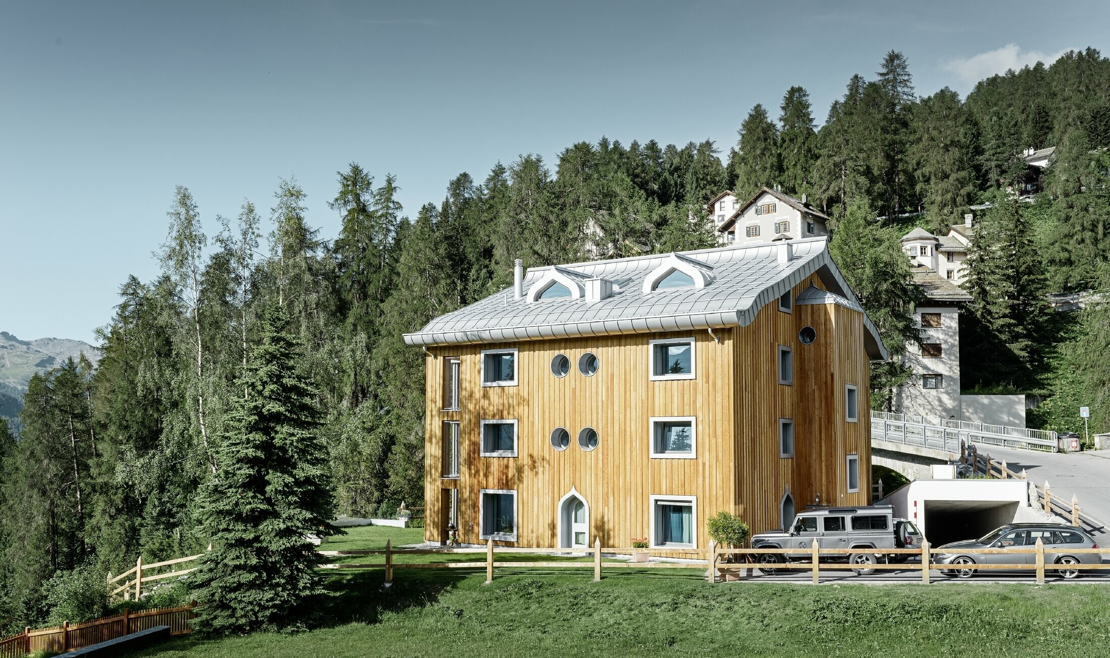 Bytový dom v St. Moritz s drevenou fasádou a hliníkovou strechou s zakriveným odkvapom vo farbe strieborná metalíza