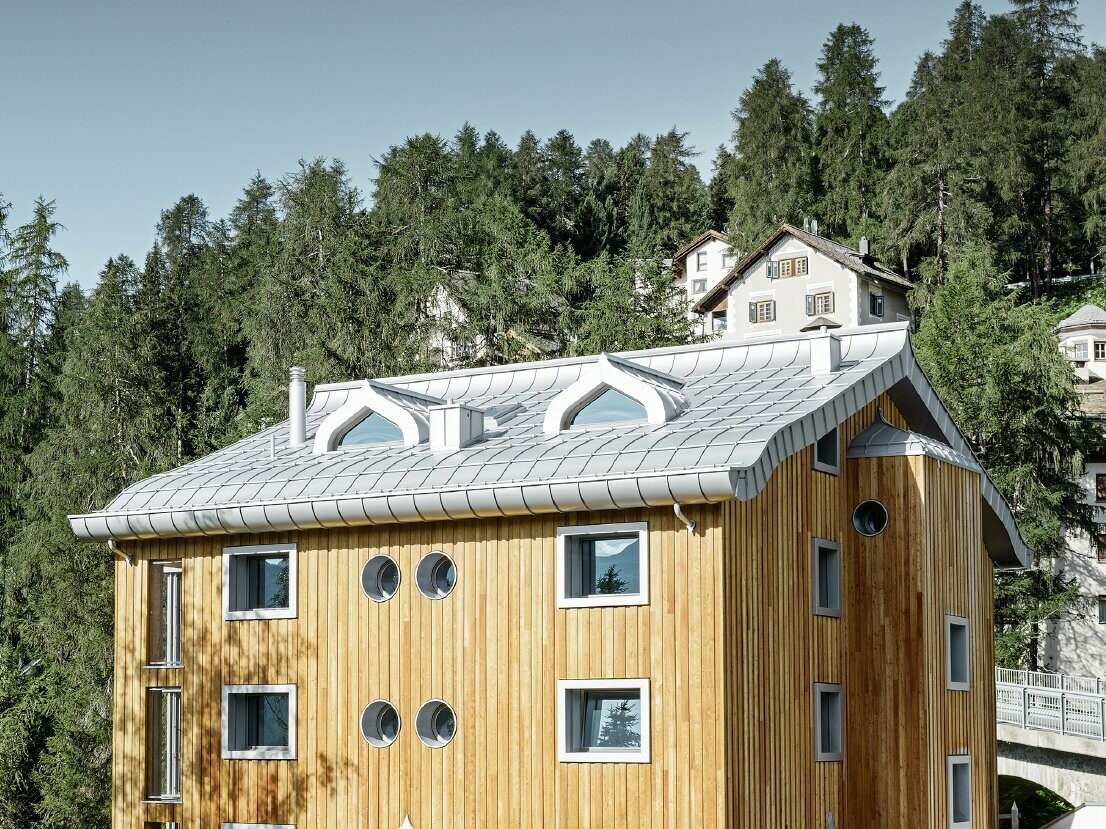 Bytový dom v St. Moritz s drevenou fasádou a hliníkovou strechou s zakriveným odkvapom vo farbe strieborná metalíza