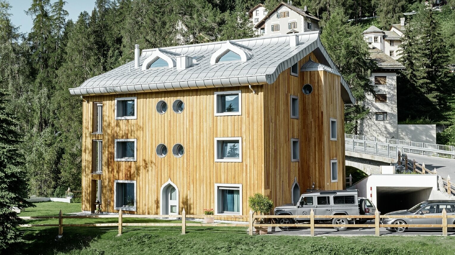 Bytový dom v St. Moritz s drevenou fasádou a hliníkovou strechou s zakriveným odkvapom vo farbe strieborná metalíza
