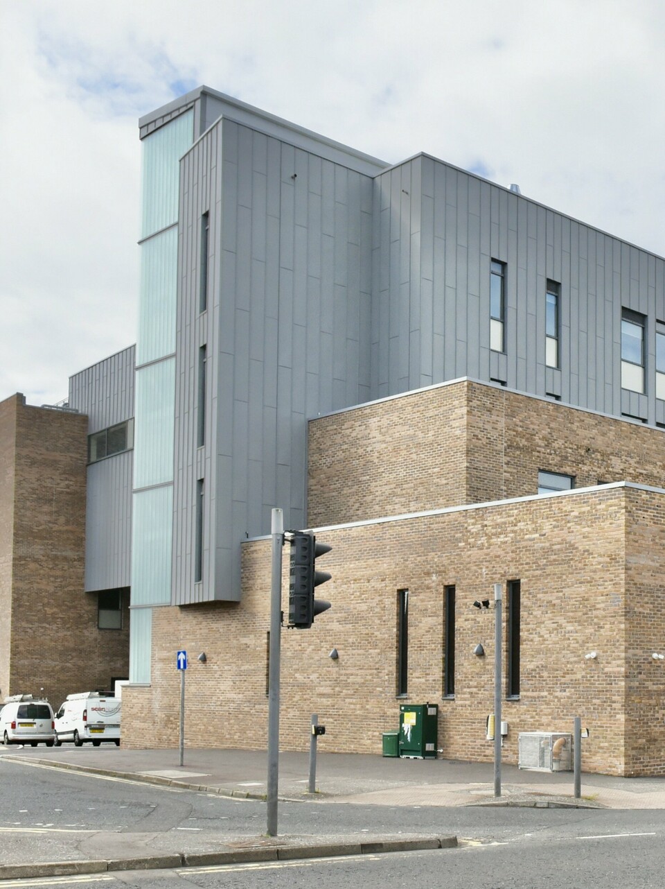 Blick auf den Zufahrtsbereich des North Regional College in Coleraine. Die PREFALZ Aluminiumfassade in Patinagrau setzt einen modernen Kontrast zur historischen Backsteinarchitektur und bietet durch die Stehfalzverkleidung dauerhafte Beständigkeit und gestalterische Eleganz.