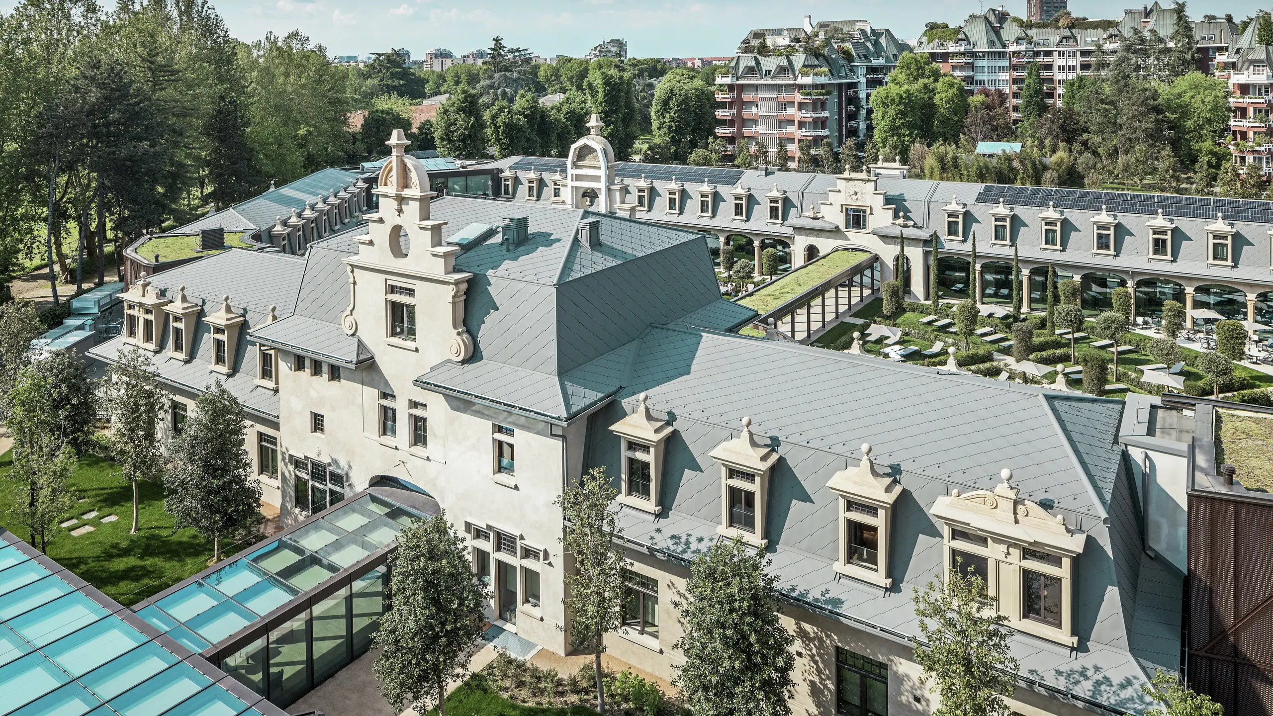 Celkový pohľad na impozantný komplex „De Montel – Terme Milano“ s pamiatkovo chránenou secesnou architektúrou a moderným wellness prostredím. Rozsiahla strešná krytina s PREFA strešnými šablónami 44 × 44 v odtieni P.10 svetlošedá dodáva komplexu elegantnú jednotnosť. Integrované fotovoltické moduly, zelené strechy a sklenené prepojenia medzi budovami odrážajú požiadavky na udržateľnosť a moderný dizajn v mestskom kontexte.