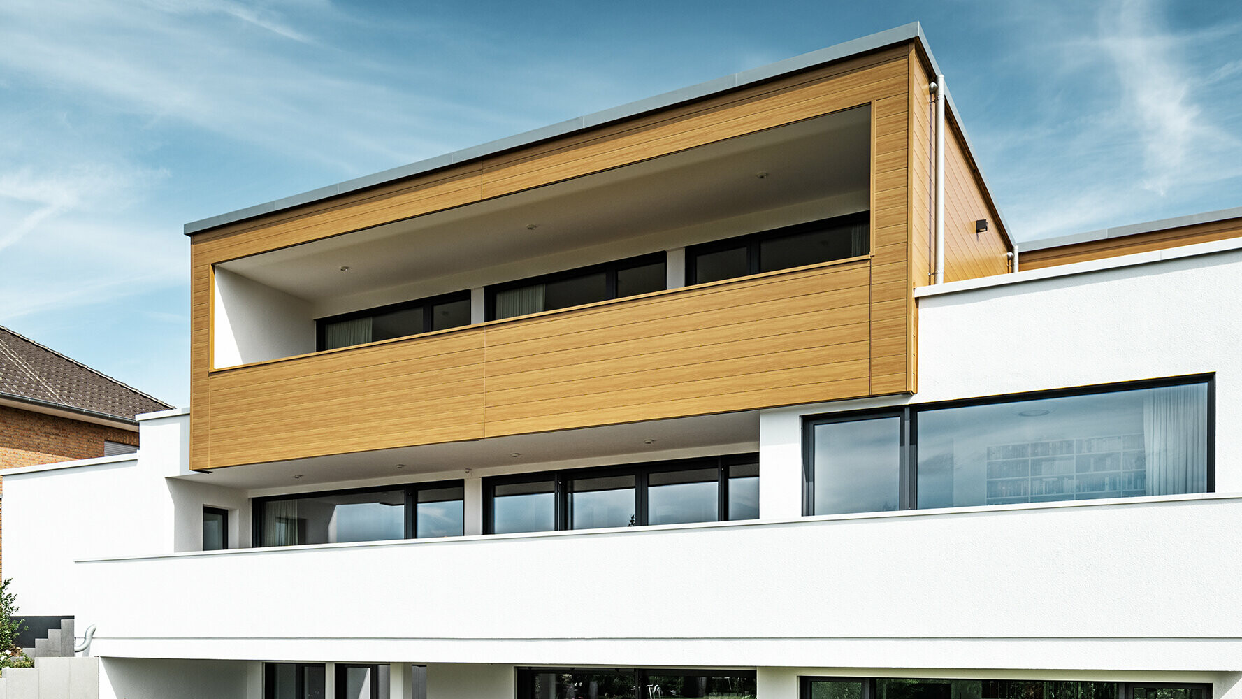 Moderná obytná budova s balkónom obloženým fasádnymi panelmi PREFA Siding v dubovo béžovosivej farbe.