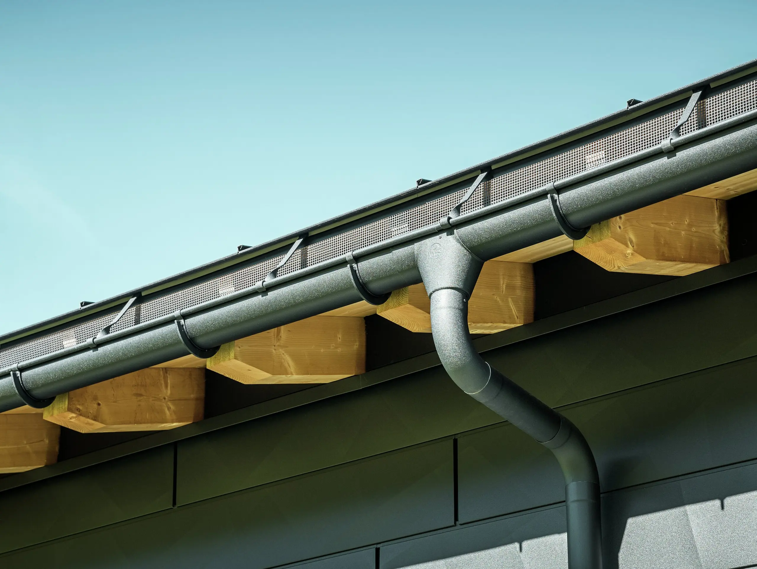 Detailný pohľad na fasádu moderného rodinného domu v Ascharine vo Švajčiarsku. Bočné steny budovy boli obložené výraznými fasádnymi panelmi PREFA Siding.X v čiernej farbe P.10. Farebne zladený je aj odvodňovací systém PREFA so žľabom a zvodom.