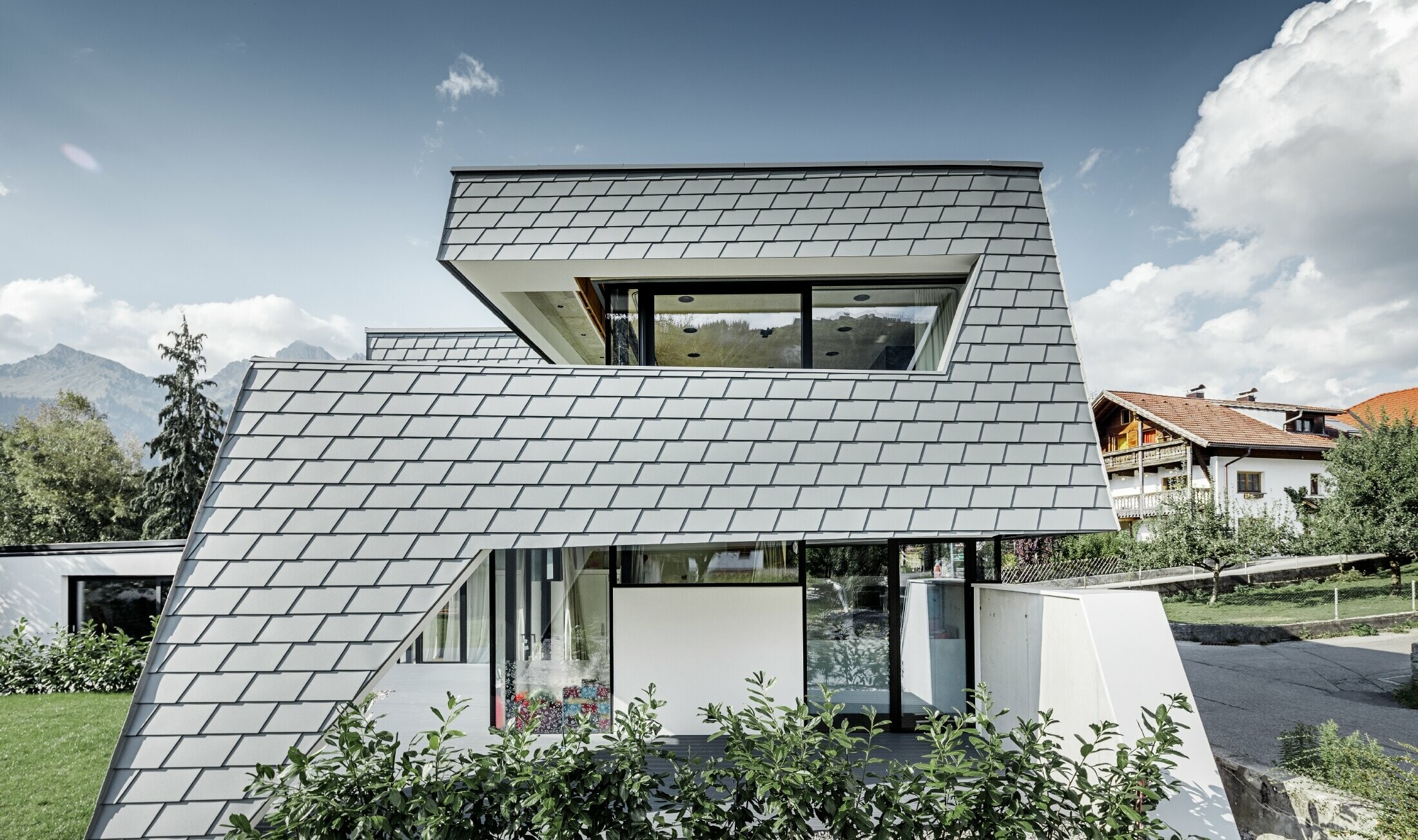 Moderný rodinný dom s plochou strechou, veľkými oknami a šindľovou fasádou v svetlošedom hliníku od firmy PREFA