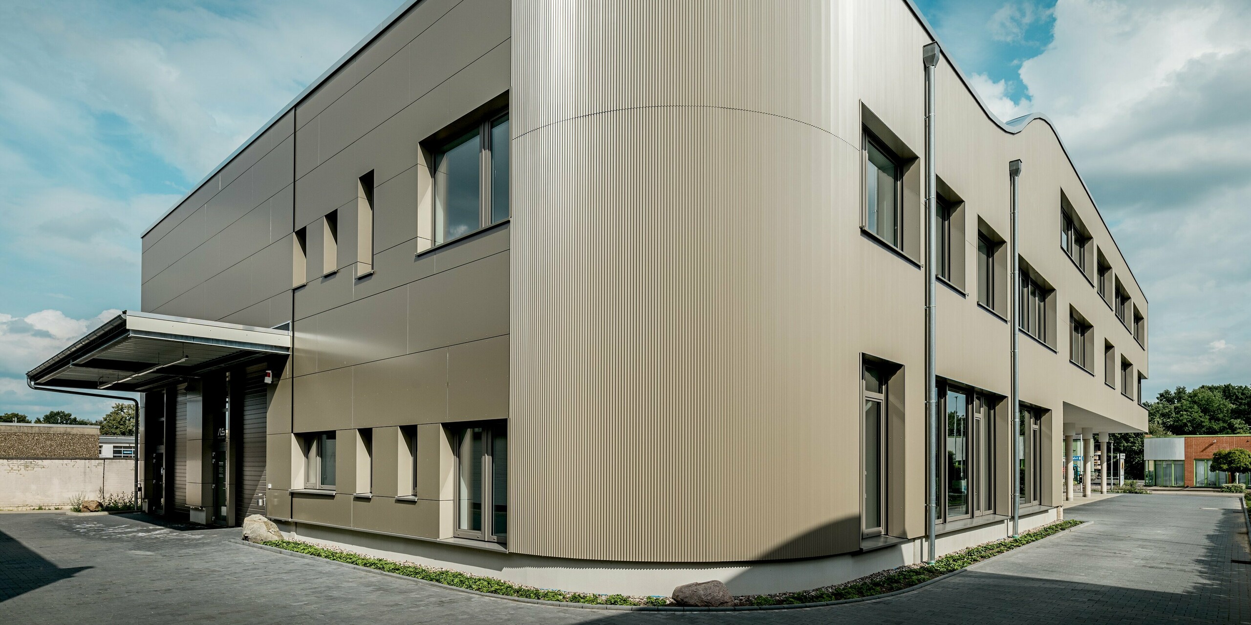 Das Bild zeigt das Festo-Gebäude in Langenhagen mit einer markanten Gebäuderundung, die mit PREFA Strangpressprofilen in Zackenform ausgestattet ist. Die harmonische Kombination aus den glatten Aluminium Verbundplatten und den strukturierten Zackenprofilen verleiht der Fassade eine moderne und dynamische Ästhetik. Besonders auffällig ist die sanft abgerundete Ecke des Gebäudes, die dem Bauwerk eine elegante, fast futuristische Ausstrahlung verleiht. Die Fenster sind präzise in die Fassade integriert, was die klare Linienführung des Designs unterstreicht. Die Verwendung der langlebigen PREFA Materialien garantiert sowohl eine ästhetisch ansprechende als auch witterungsbeständige Lösung für moderne Architektur.